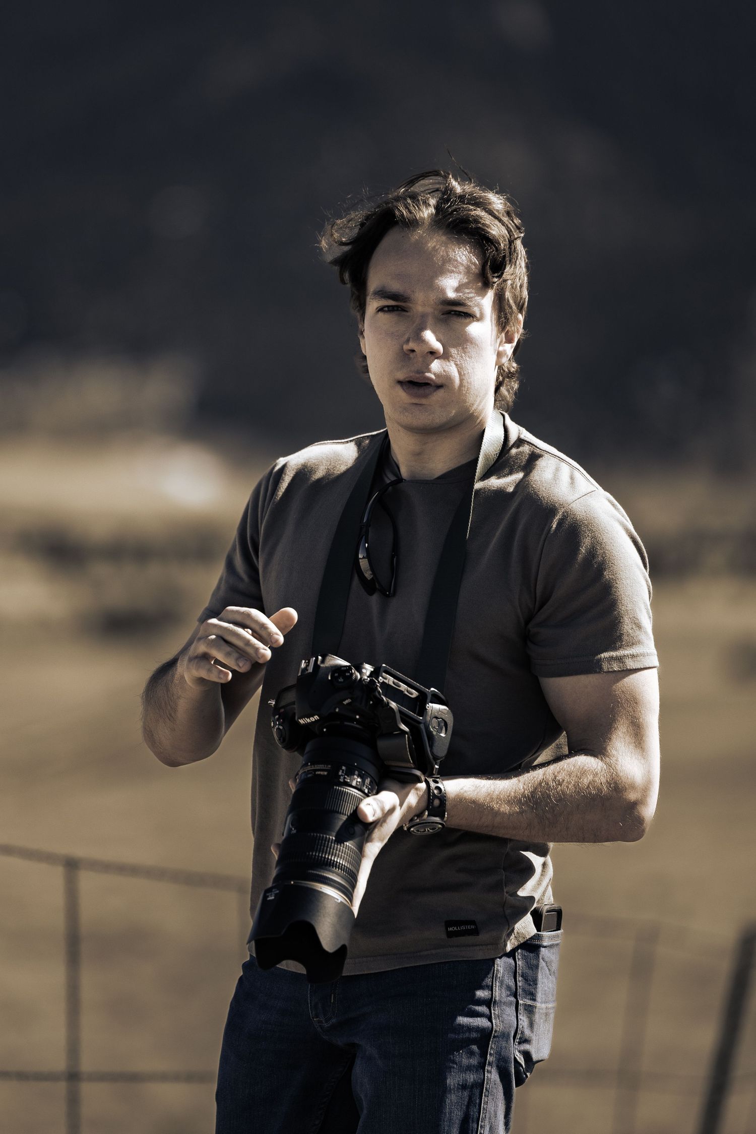 Photographer in dark clothing holding a camera outdoors in sepia tones.