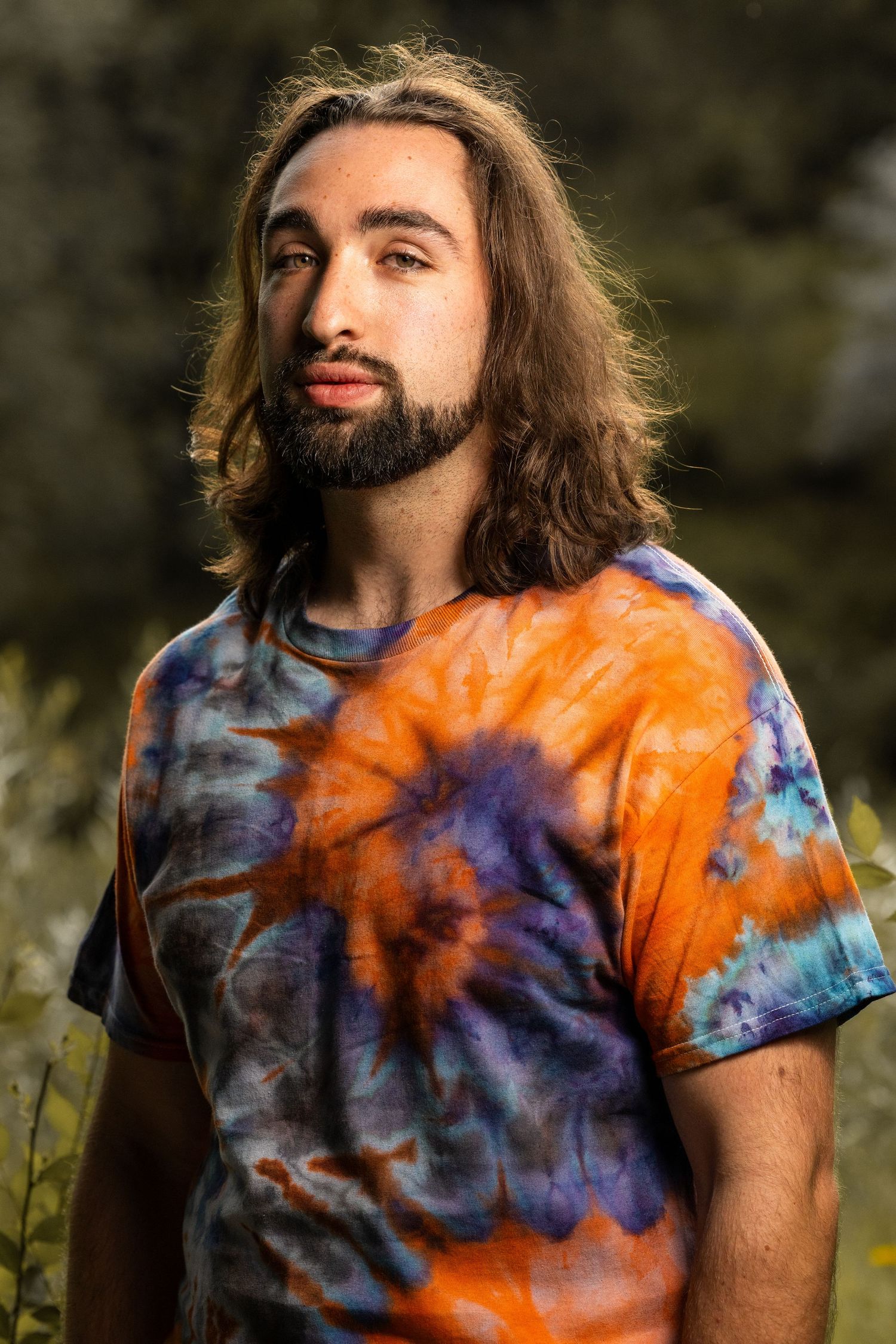 Portrait of someone wearing an orange and purple tie-dye shirt against a natural outdoor background.