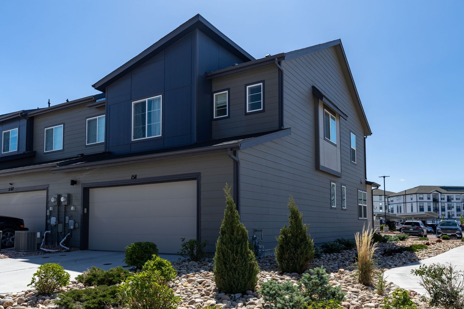 Modern two-story townhome with dark blue and gray siding, attached two-car garage, and landscaped front yard.