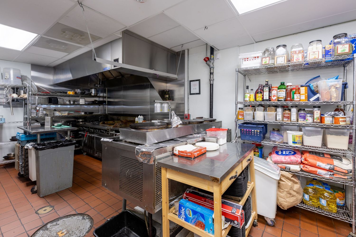 Well-equipped commercial kitchen with stainless steel prep tables and storage shelves.