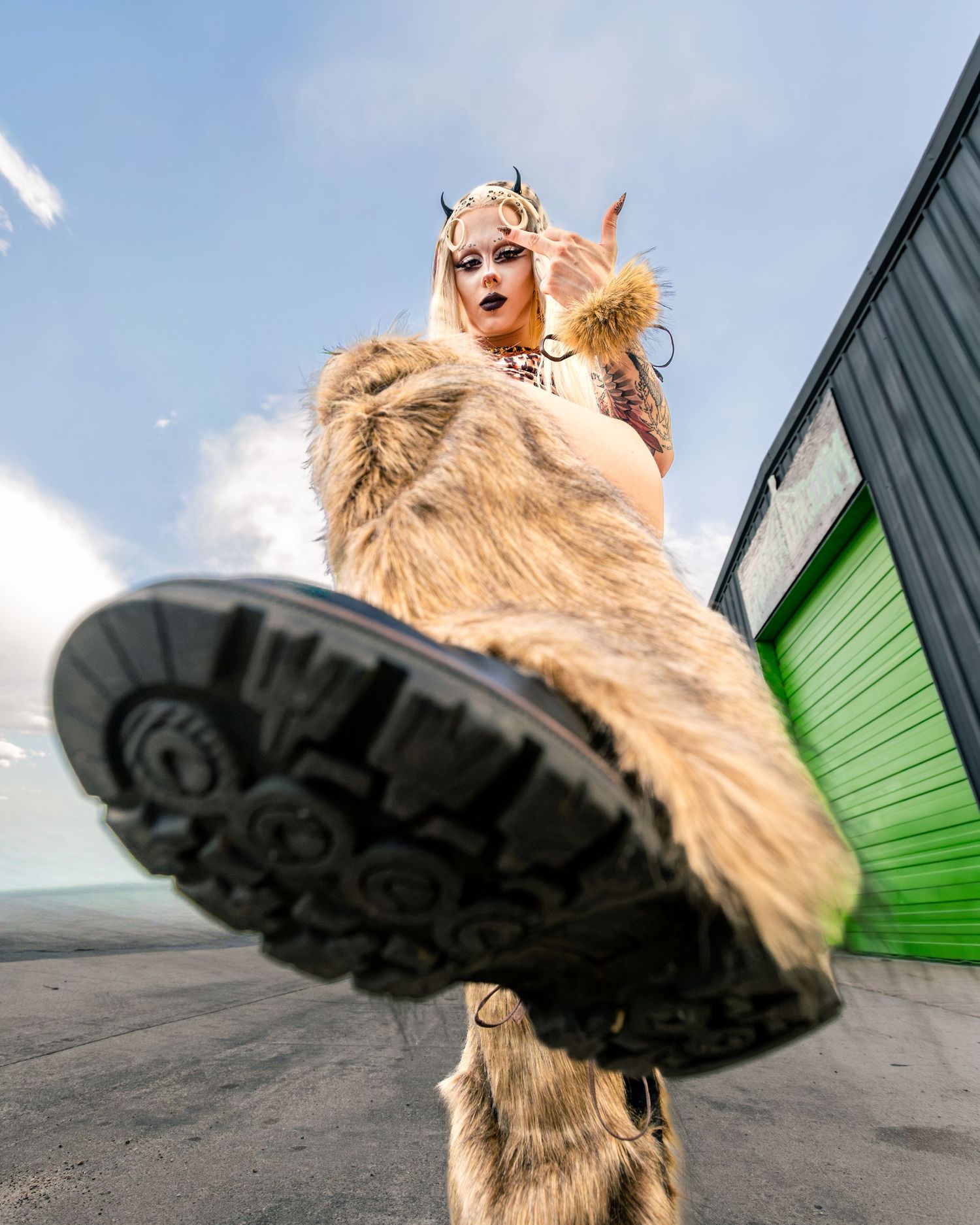 Low angle shot of tattooed blonde in fur costume with horns kicking toward camera outdoors.