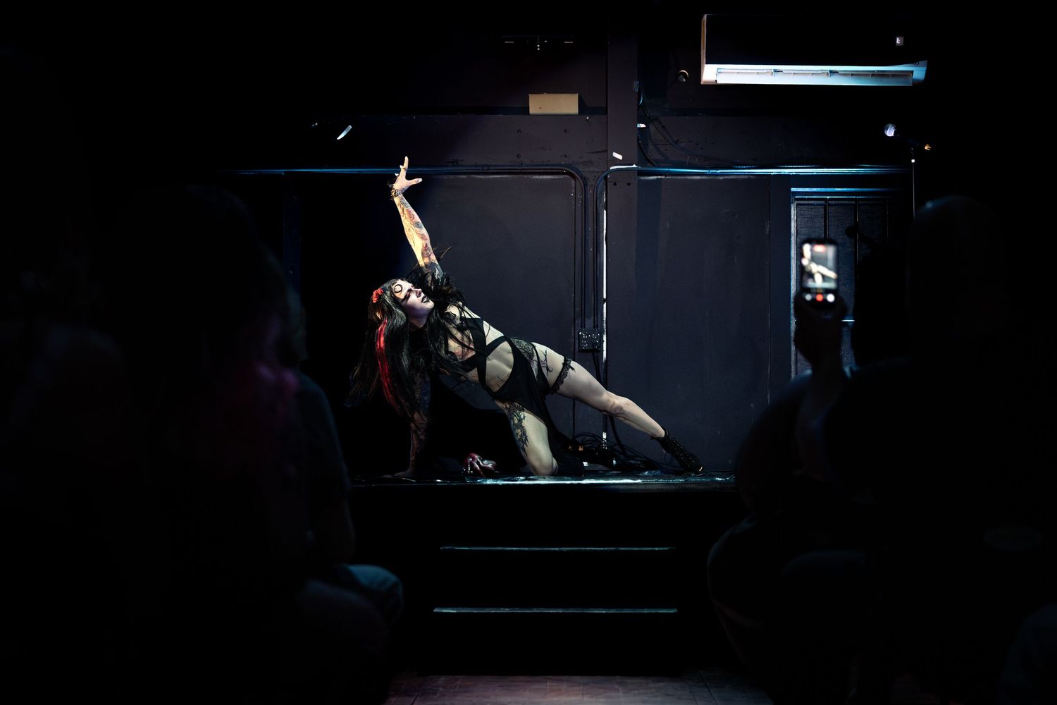 Dramatic performer in red hair strikes a pose on a dark stage under spotlight during a theatrical show.