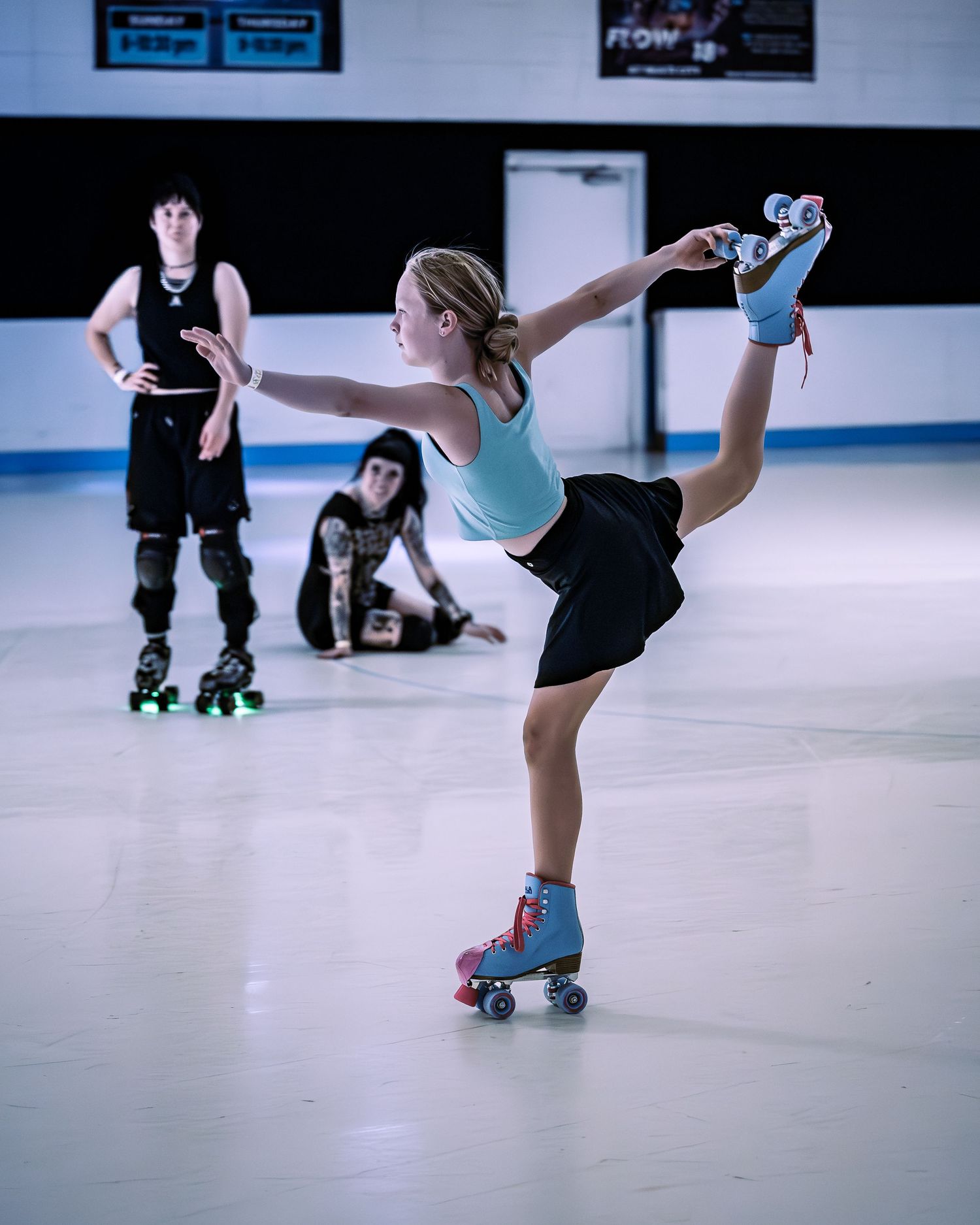 Young woman in blue top gracefully balancing on roller skates with leg raised high.