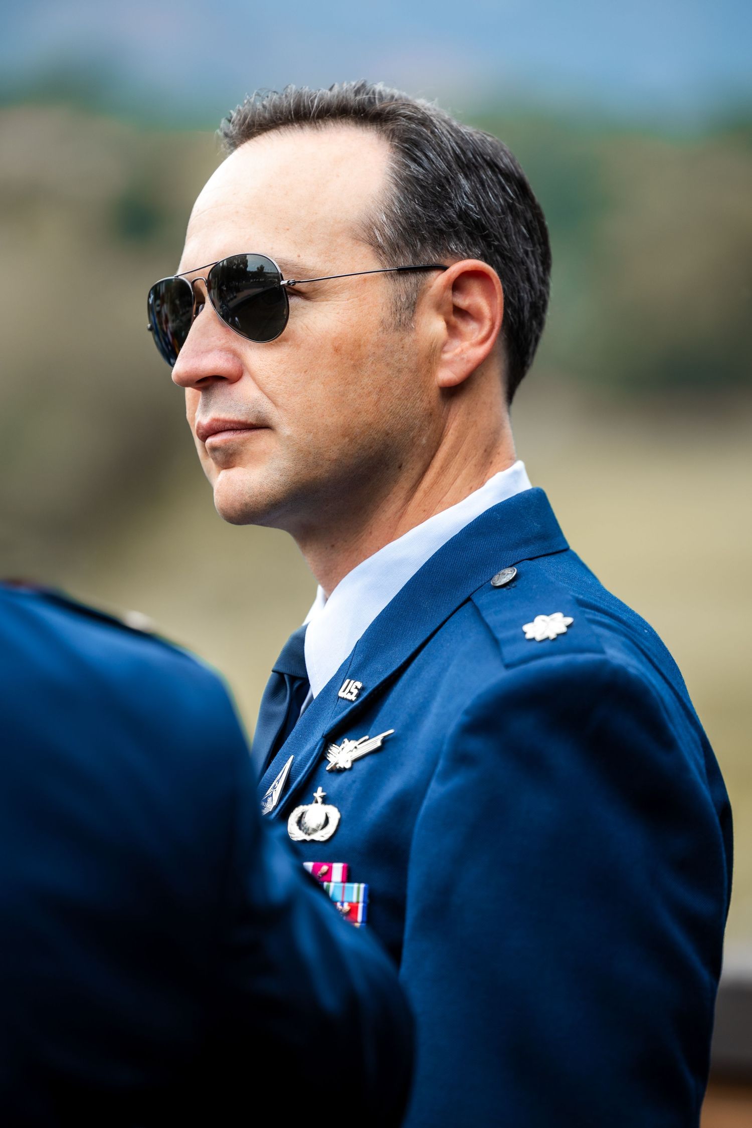Air Force service members in dress blues wearing sunglasses stand at attention outdoors.