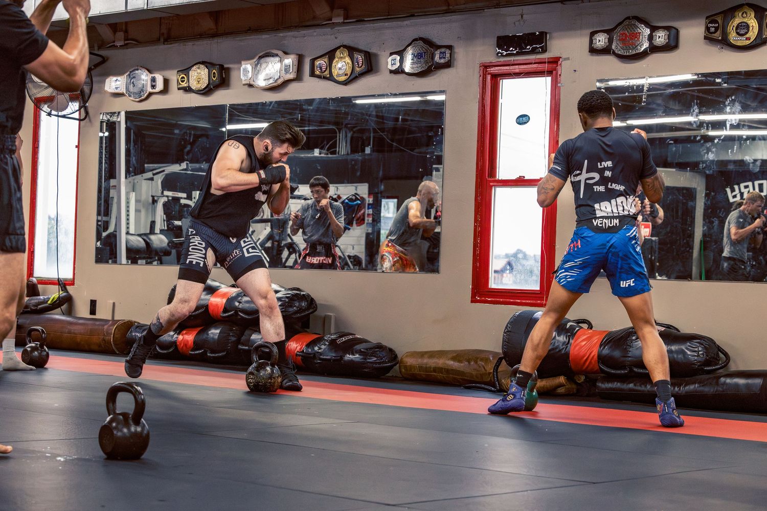 Wide view of a martial arts gym showing training equipment, championship belts, and practitioners in action.