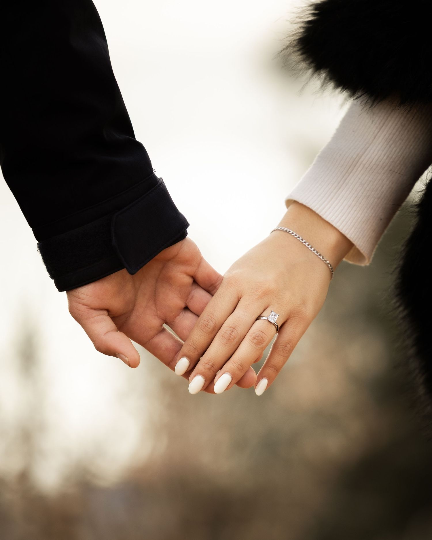 Two hands holding each other with wedding rings visible against a soft blurred background.