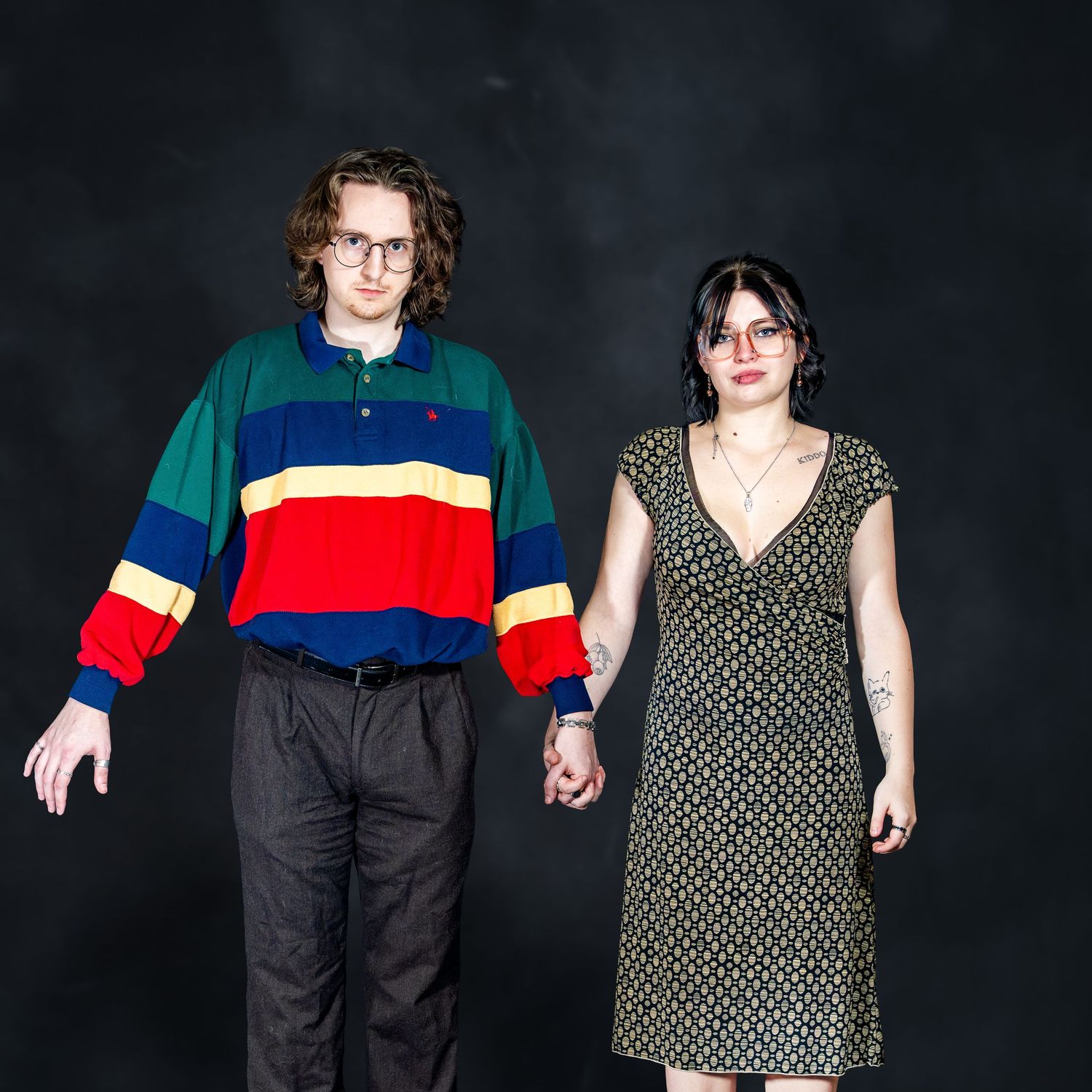 A couple holding hands in a studio, man in colorful striped polo and woman in green floral dress.