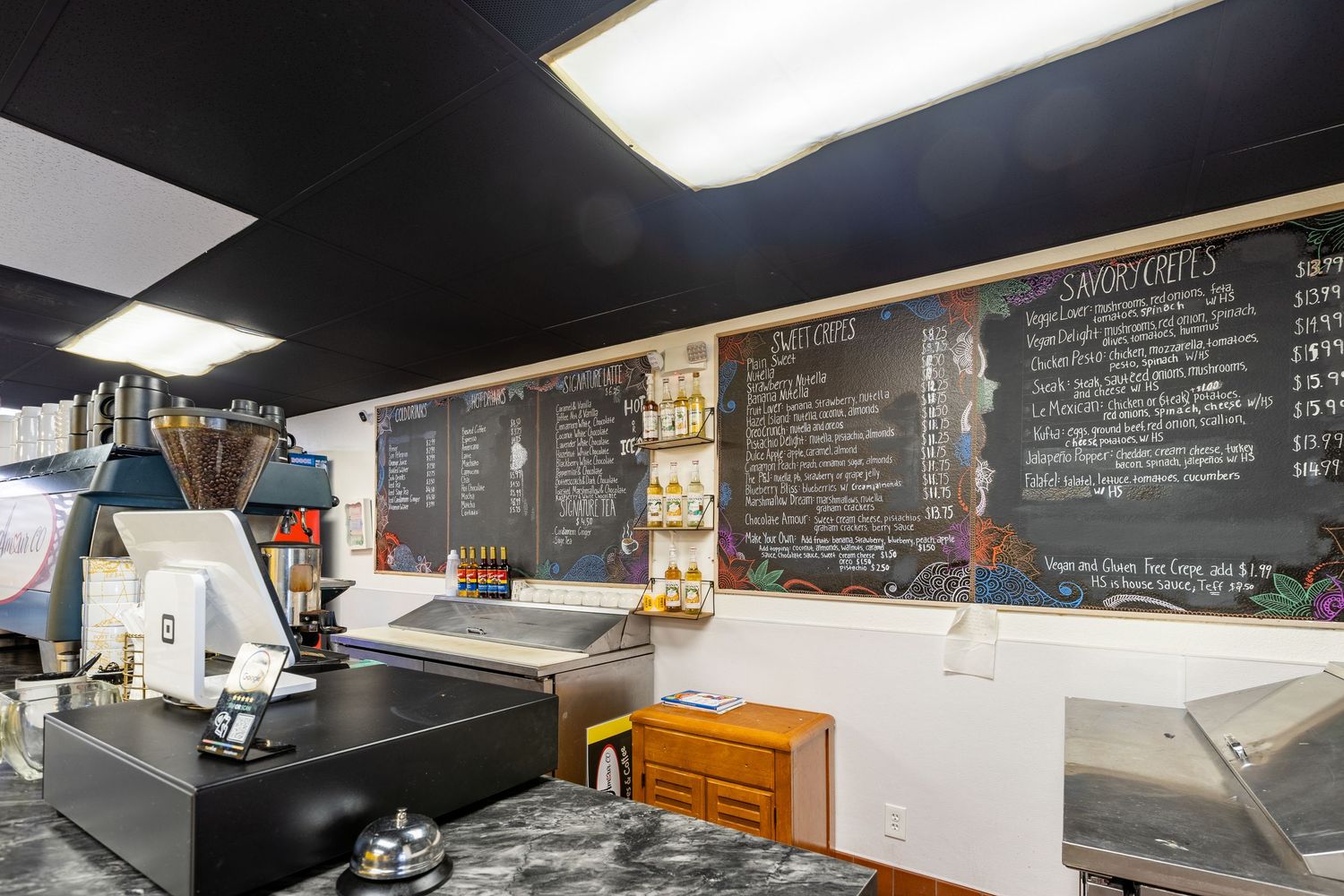 Interior of a cafe with a large chalkboard menu on the wall and a POS system on the counter.