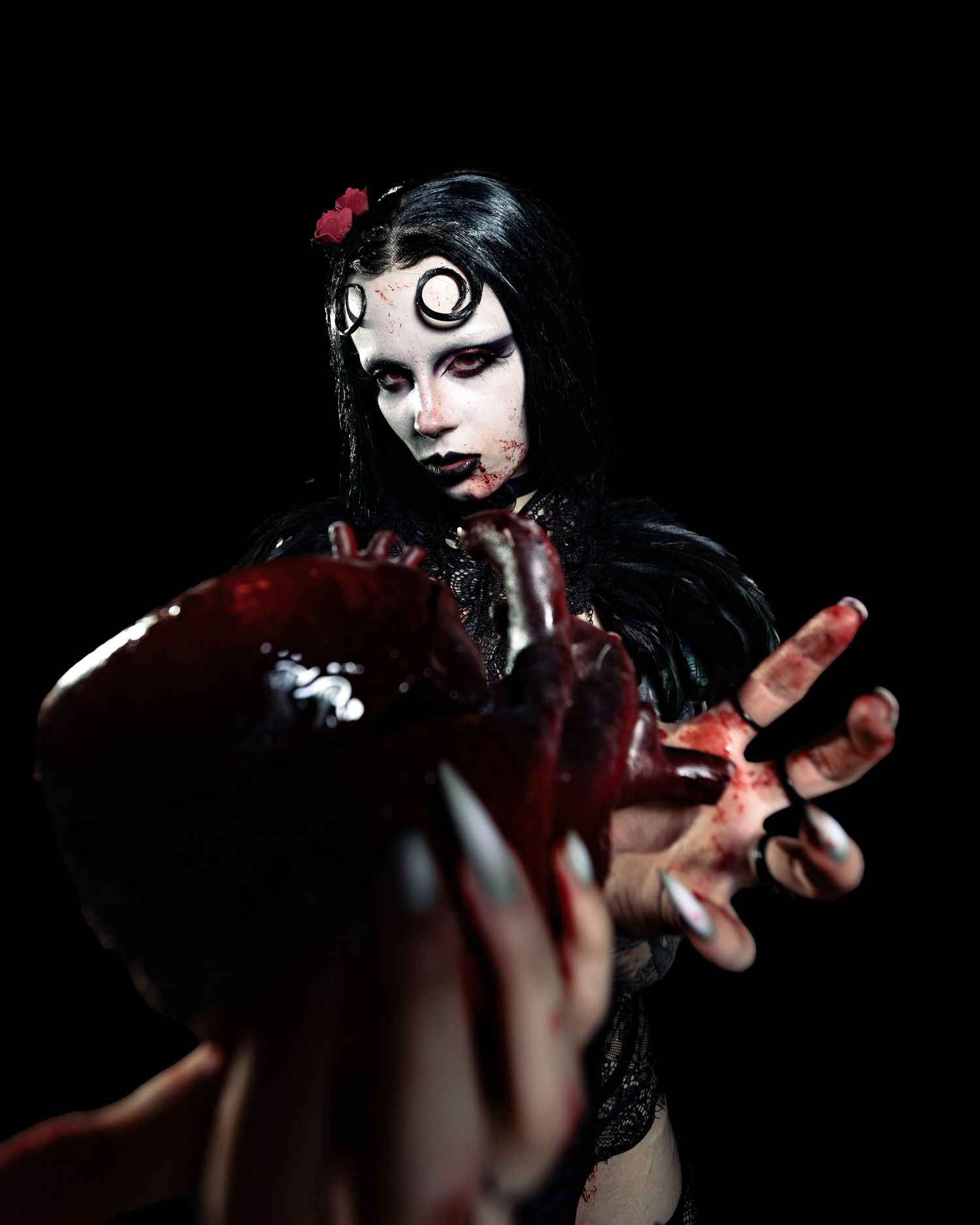 Gothic horror cosplay with dramatic white eye makeup, black feathers, and bloody hands reaching toward camera.