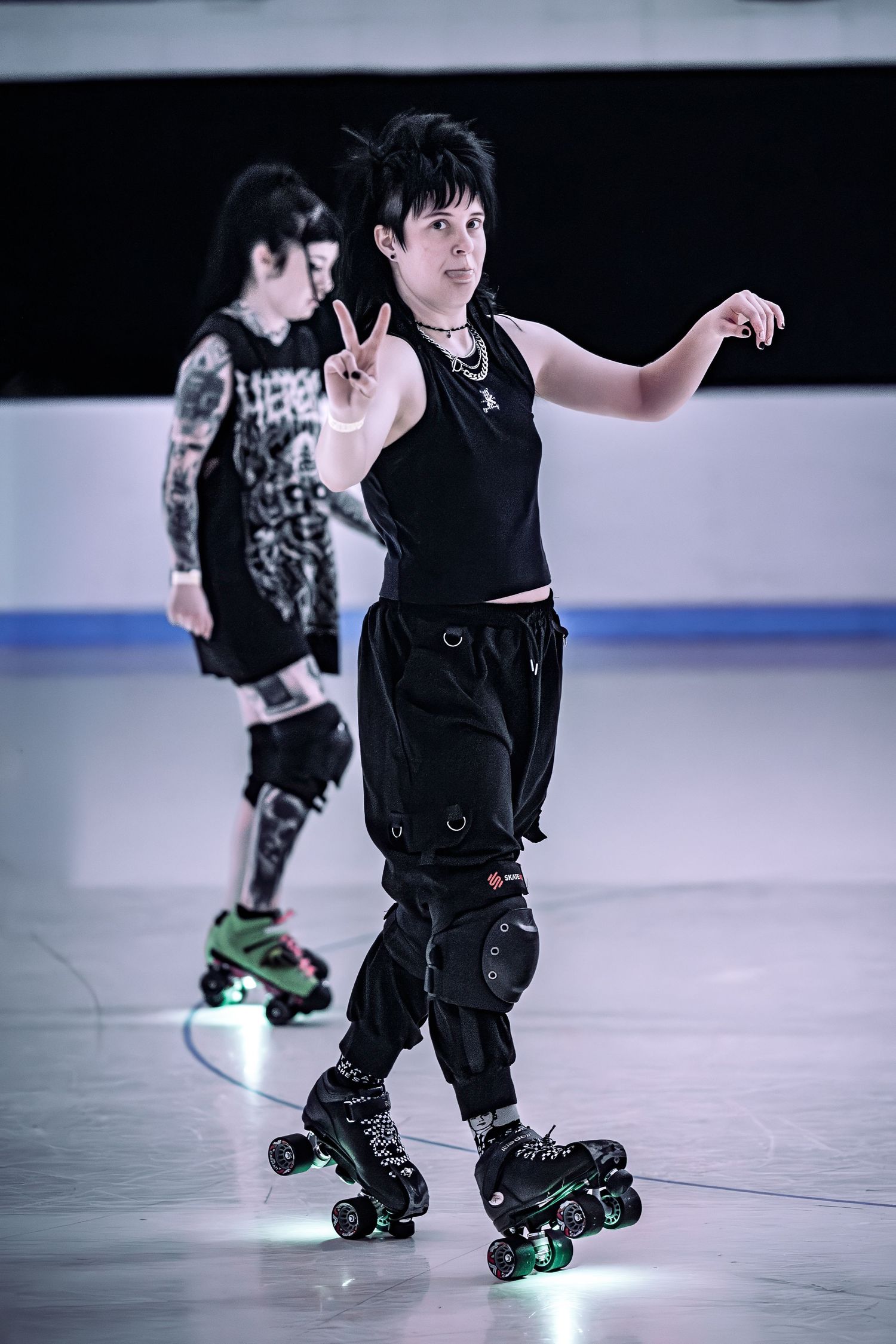 Person in black outfit performing roller skating moves with peace sign gesture indoors.