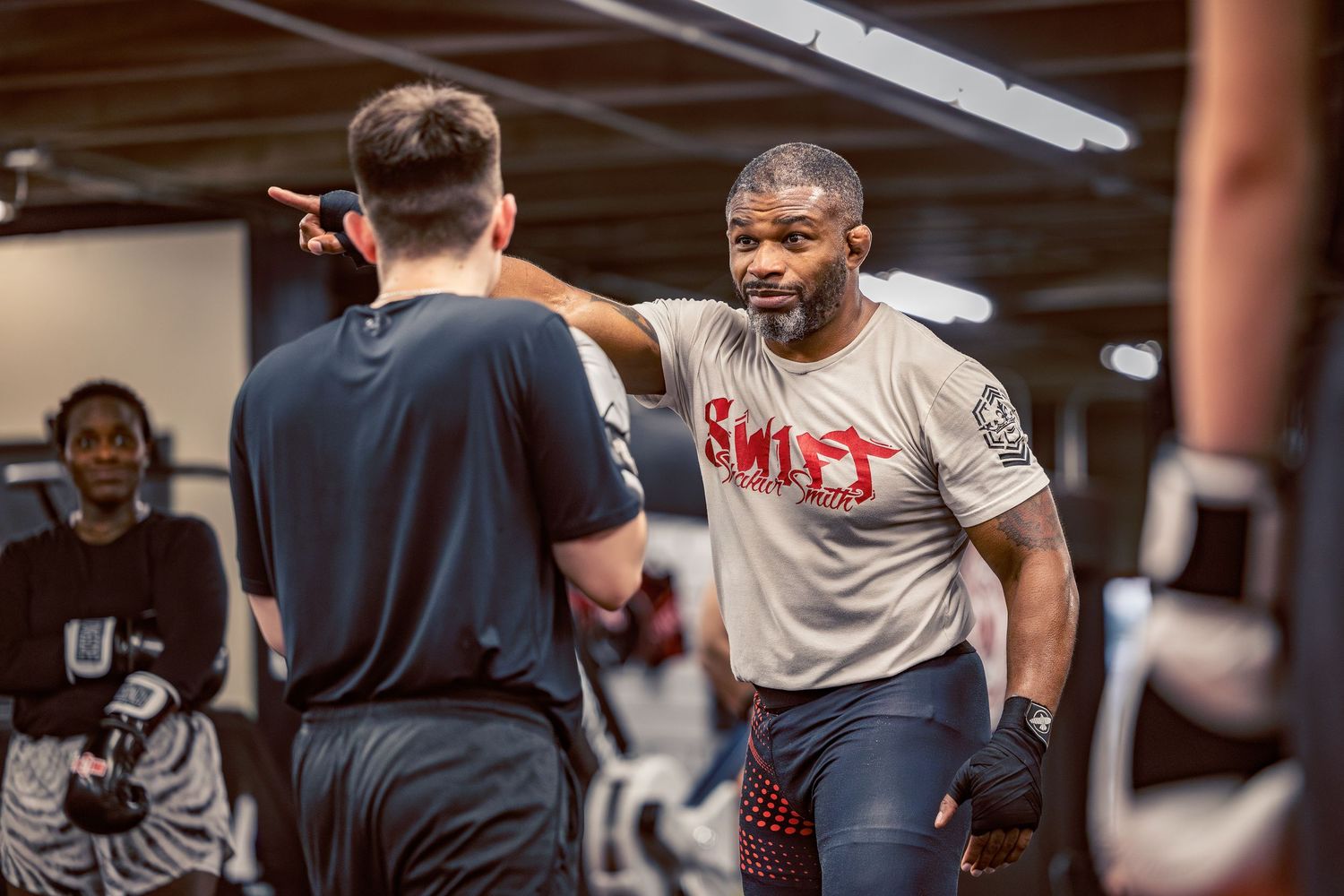 Training session in a martial arts gym with fighters practicing striking techniques and defensive moves.