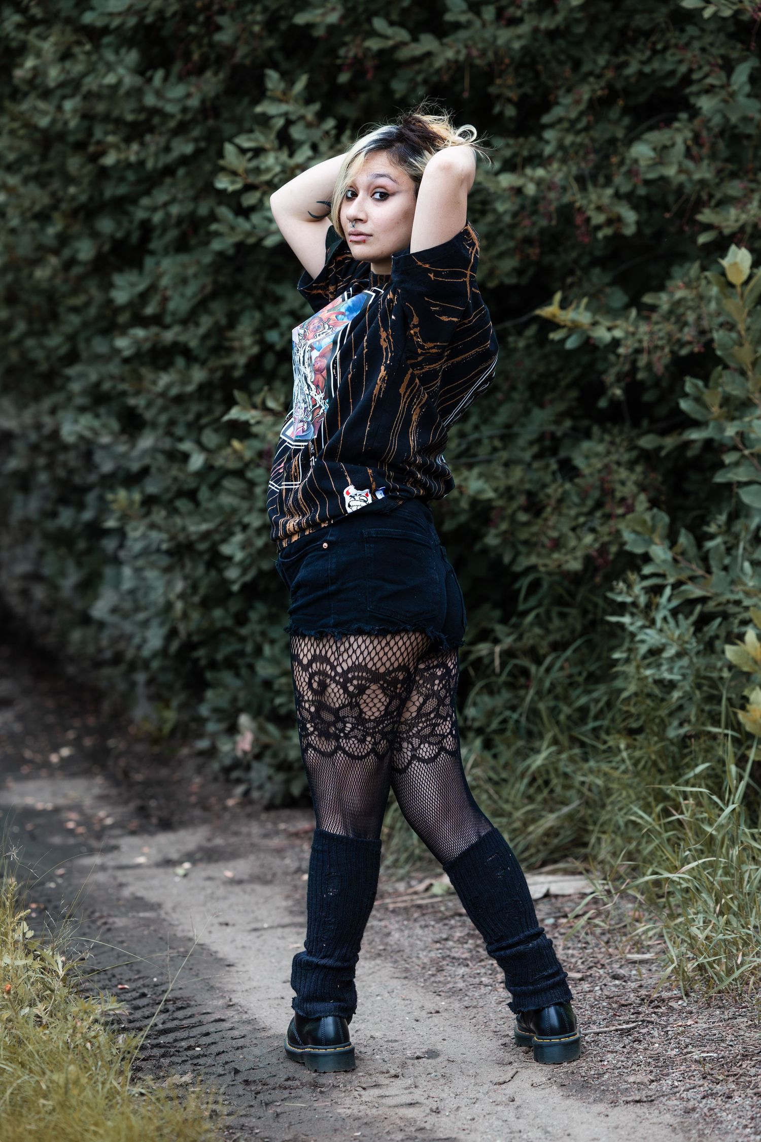 Model in black ensemble strikes dynamic poses on dirt trail.