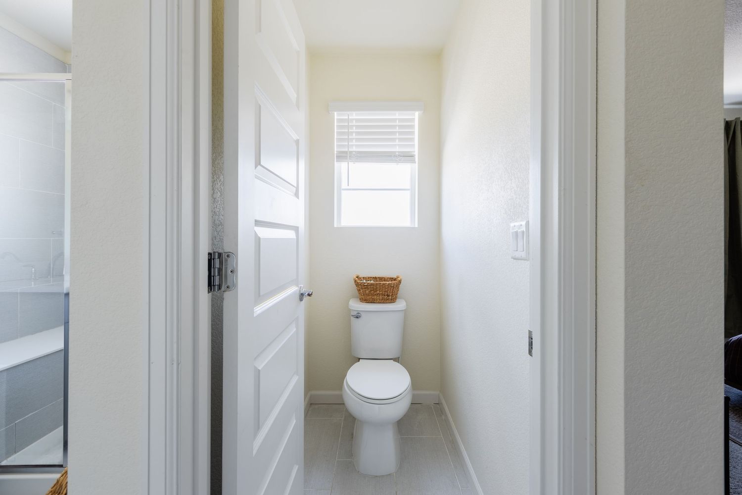 Clean narrow bathroom with white toilet, tiled floor, and small frosted window.