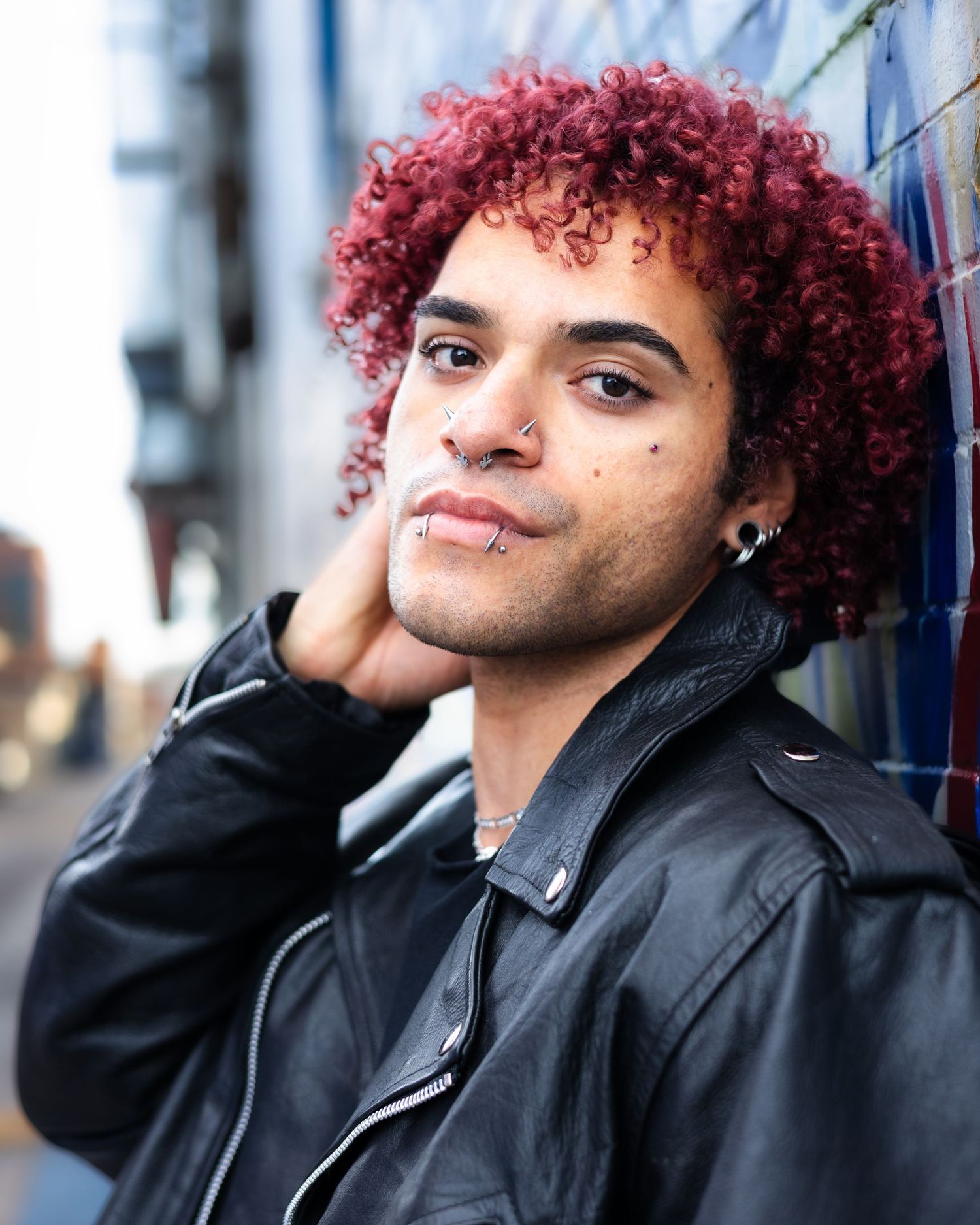 Close-up shot of person with vibrant red curly hair wearing black leather jacket.