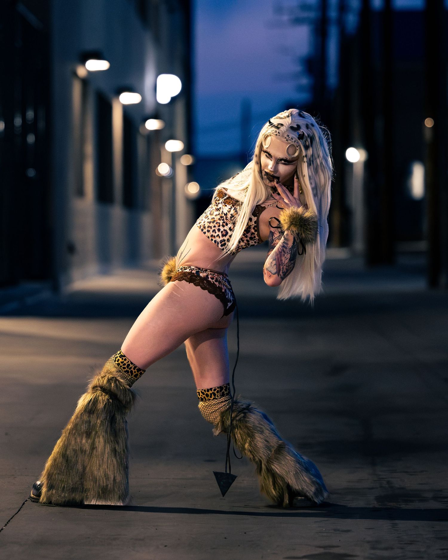 Tattooed woman in leopard costume with fur boots striking pose in night alley.