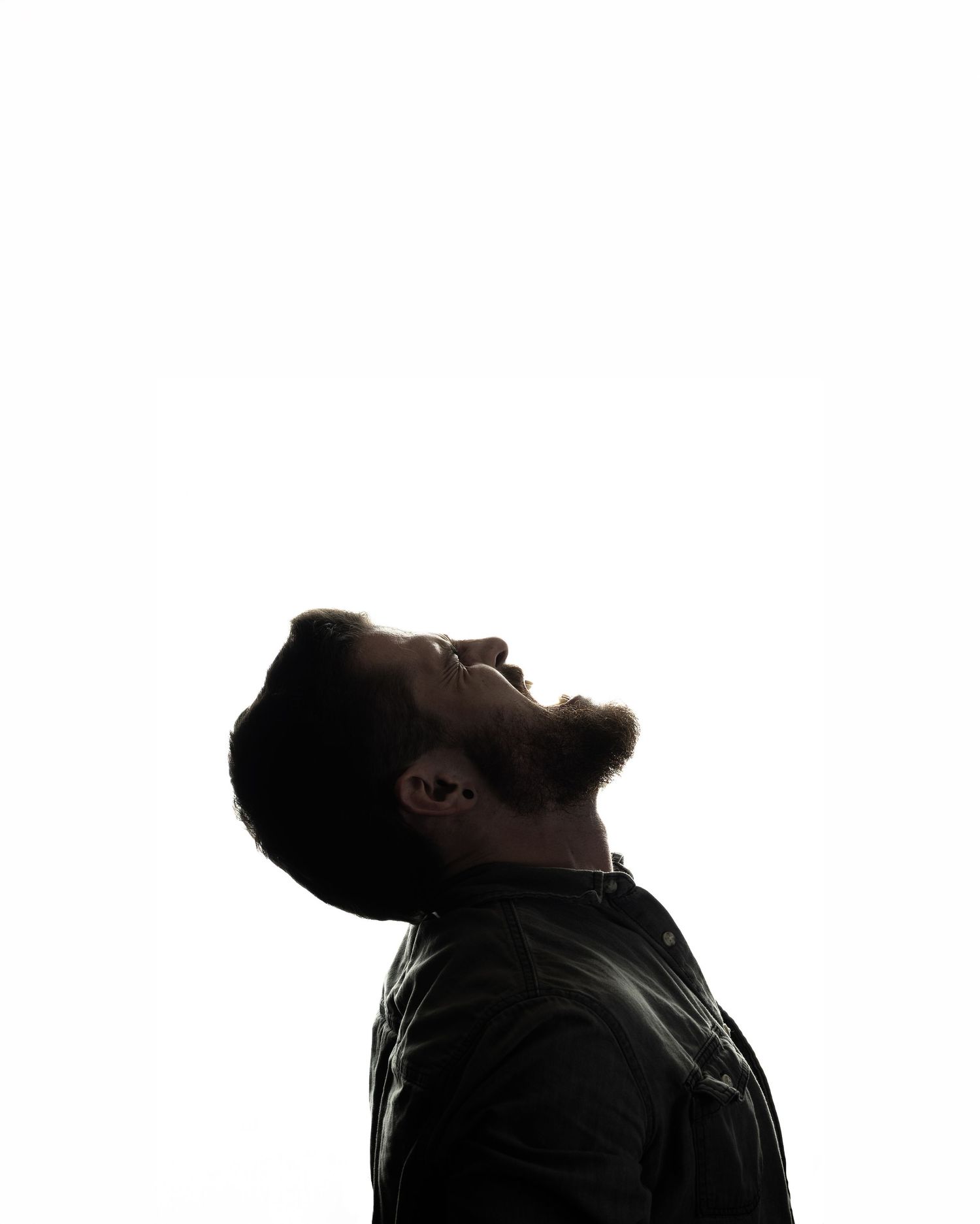 Man with beard looking upward in dramatic side profile silhouette against white background.