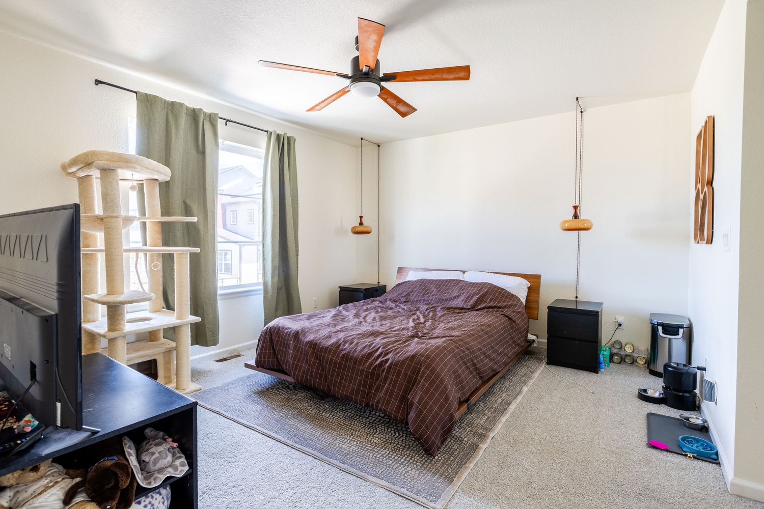 Spacious bedroom with ceiling fan, large bed, carpet flooring, and natural window light.
