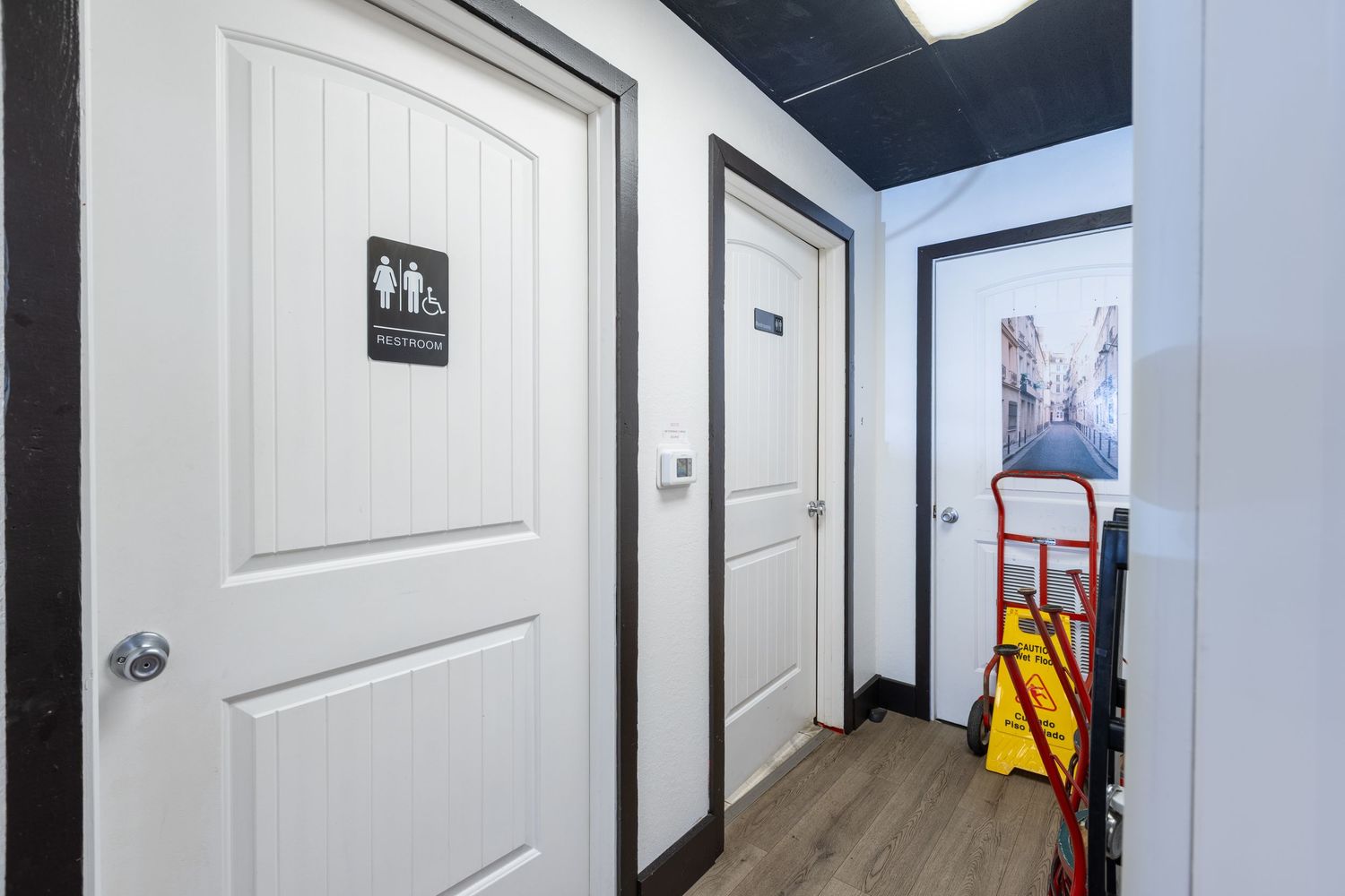 Restaurant restroom hallway with white panel doors, gender-neutral signage, and a yellow mop bucket.
