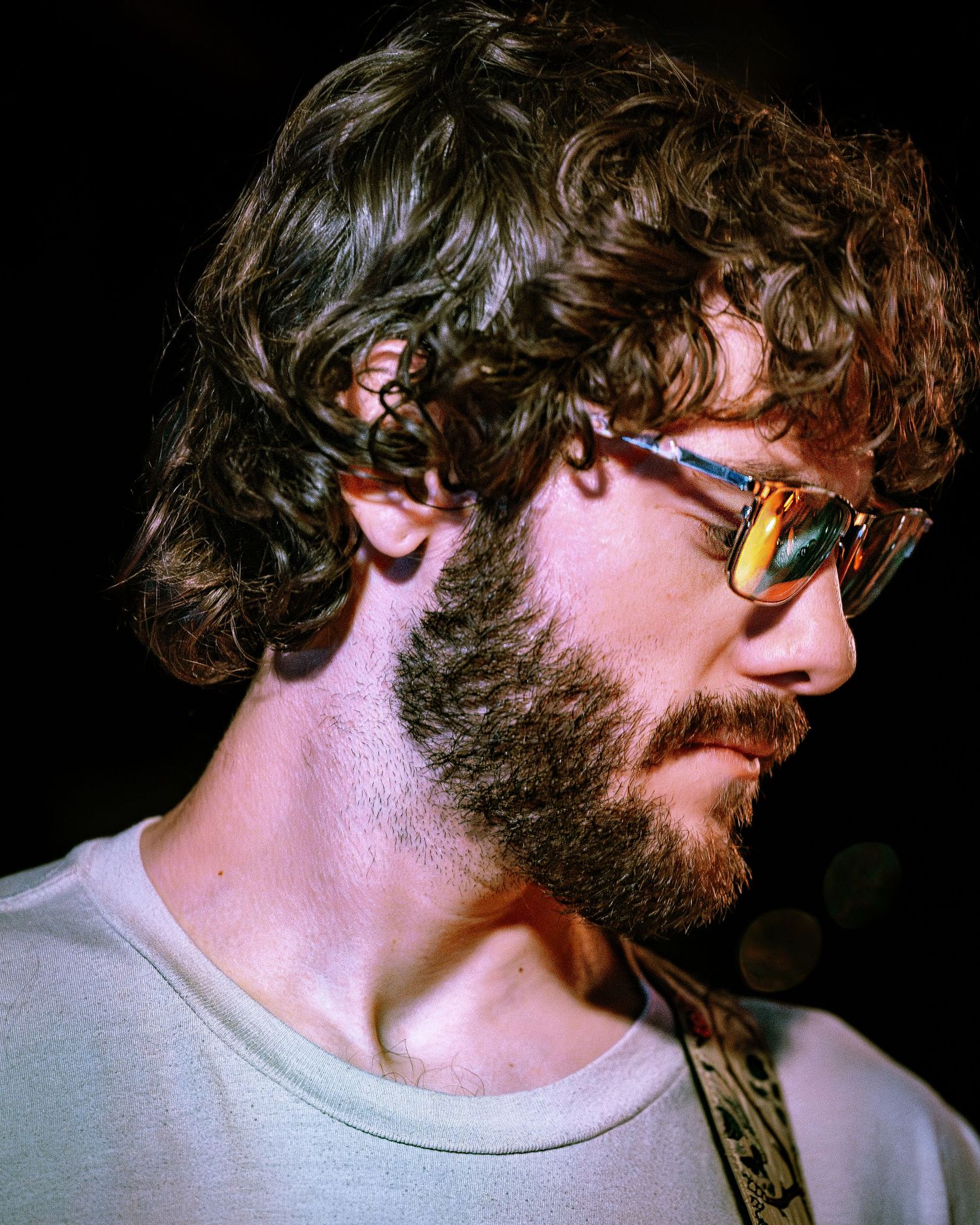 Young bearded man with curly hair wearing reflective sunglasses in warm light.