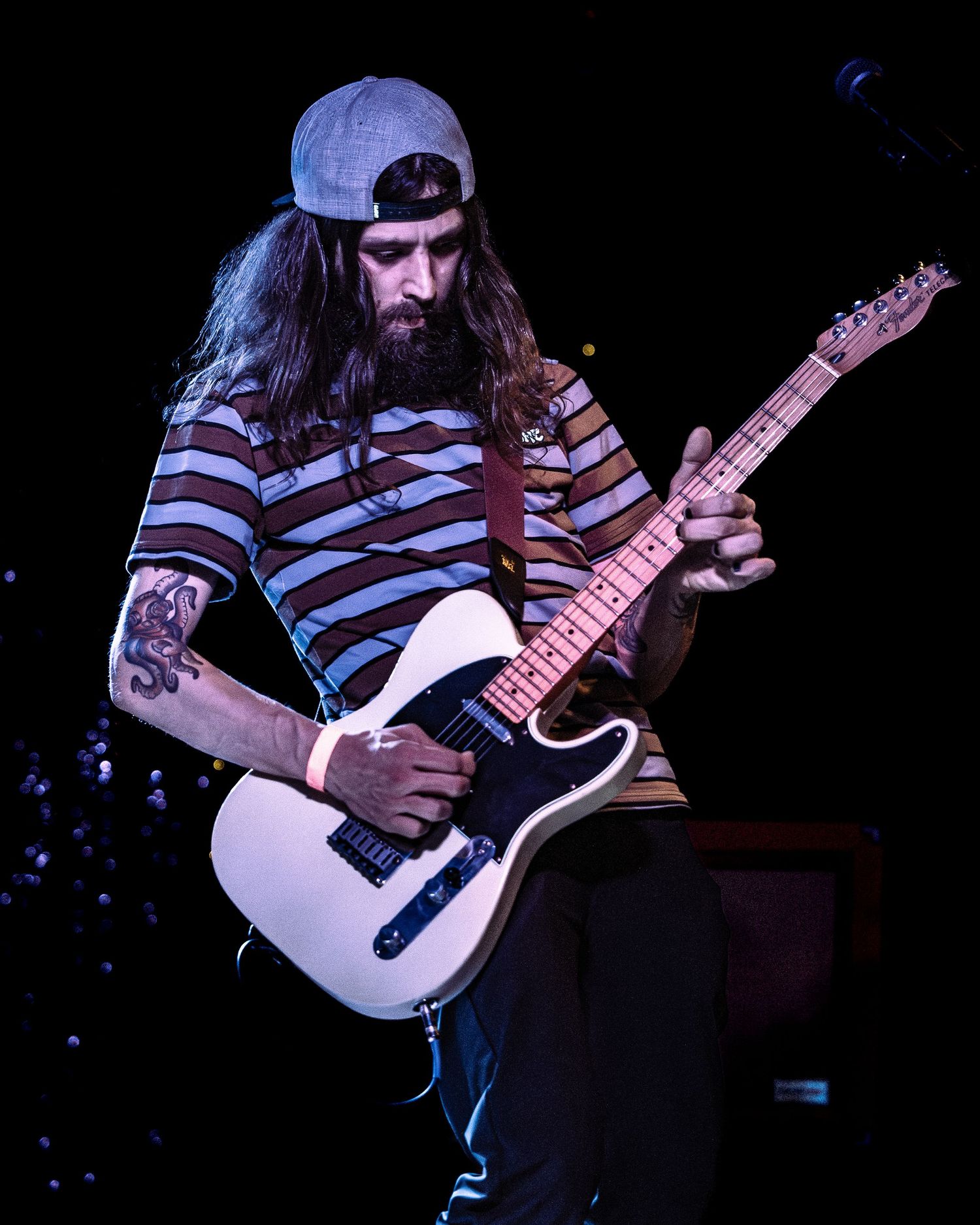 Bearded guitarist with long hair playing white Telecaster guitar on stage.
