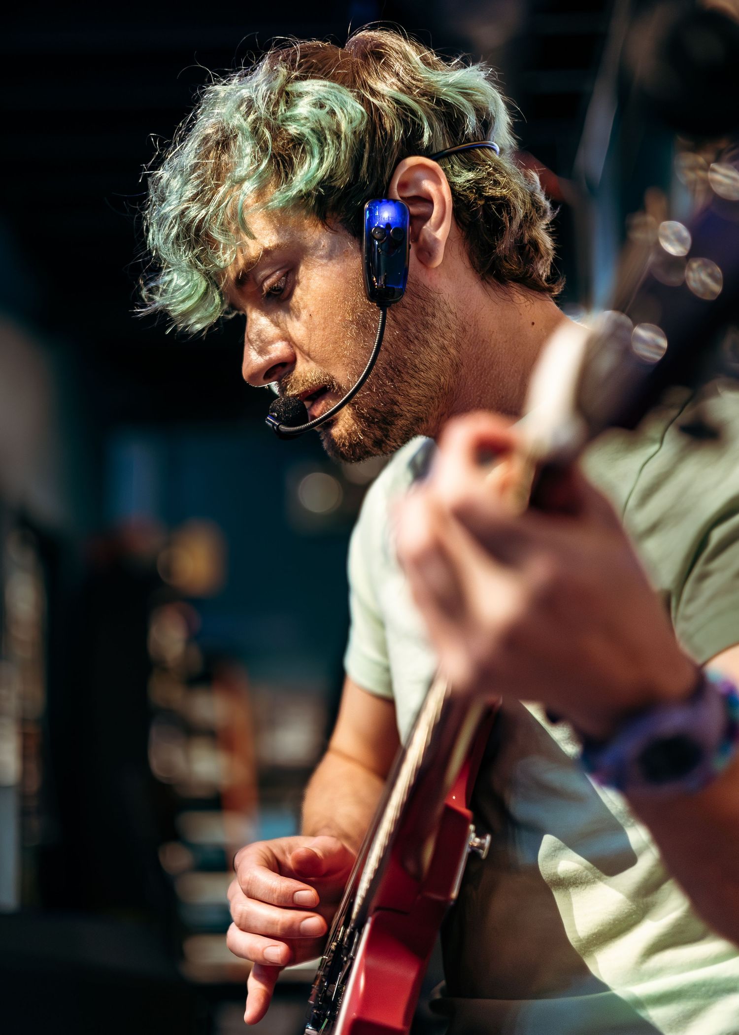 A musician wearing headphones plays a red electric guitar during a performance in a dimly lit setting.