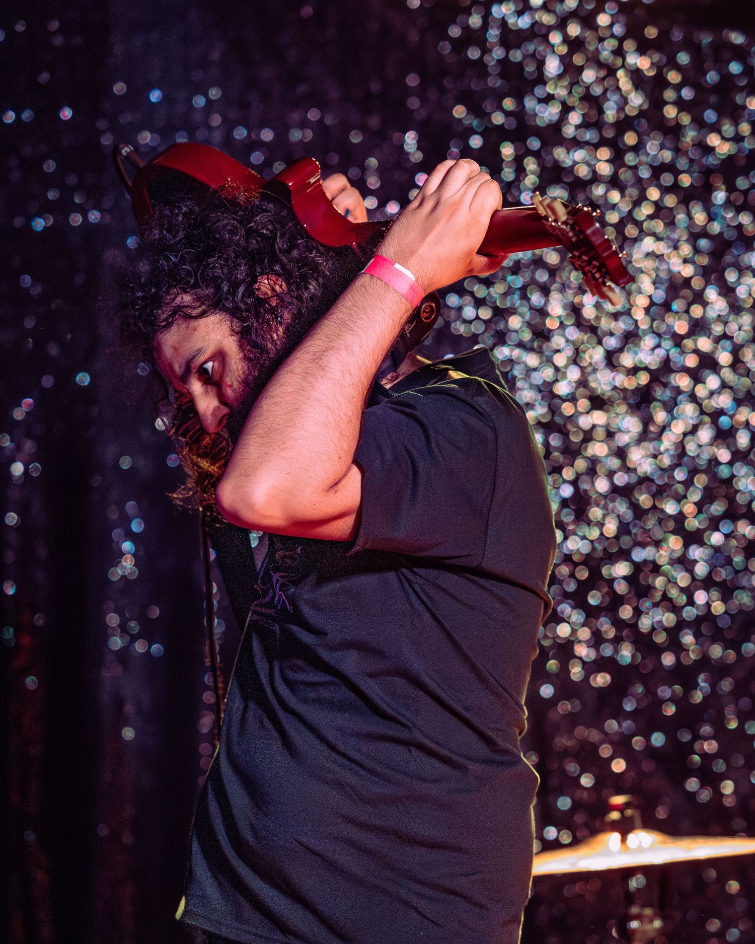 Curly-haired guitarist buries face in red guitar during an energetic live stage performance.