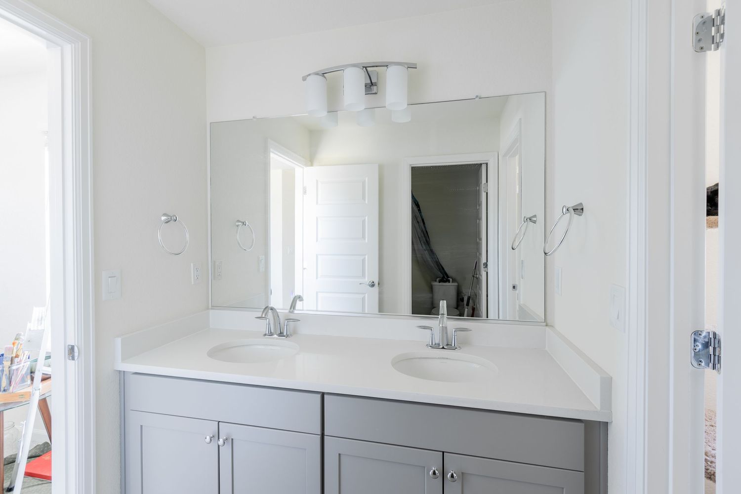 Modern bathroom with double gray vanity, white quartz countertop, dual sinks, large mirror, and bright overhead lighting.