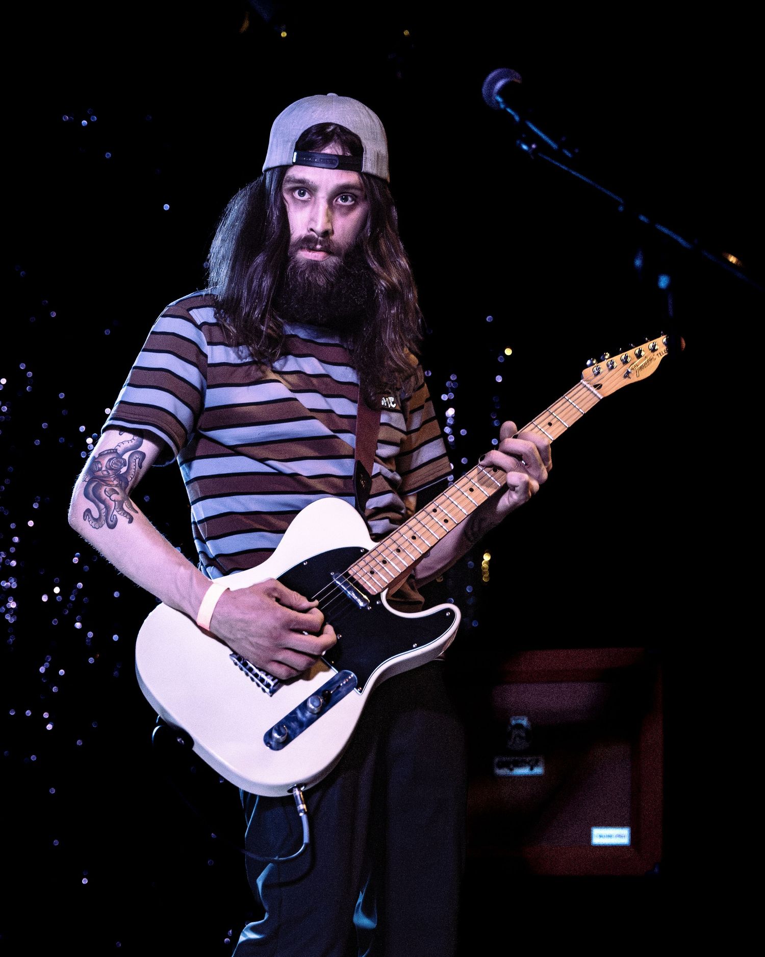 Bearded guitarist with long hair playing a white Telecaster guitar on stage.