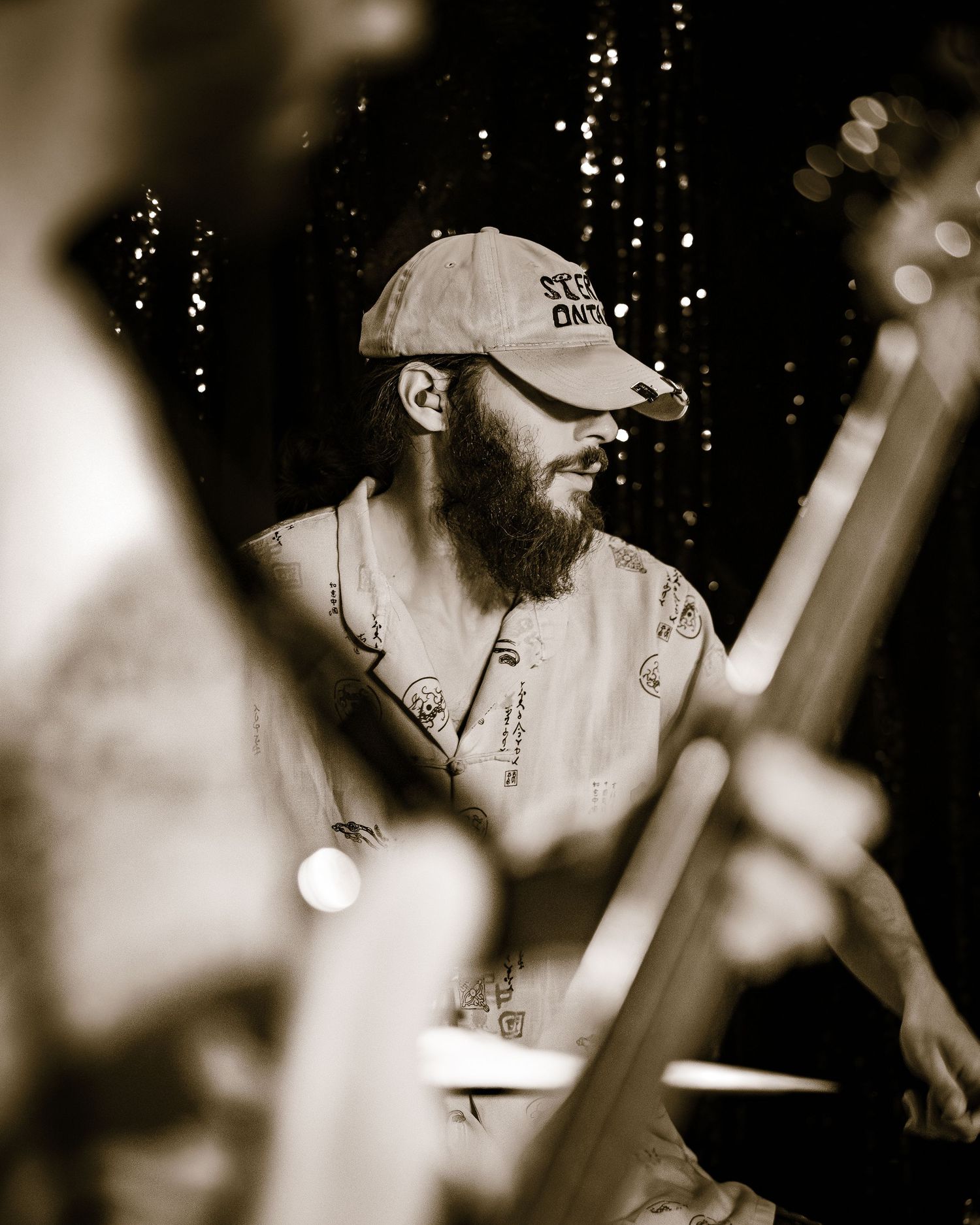 A bearded male musician wearing a cap plays guitar on stage in a sepia-toned concert photo.