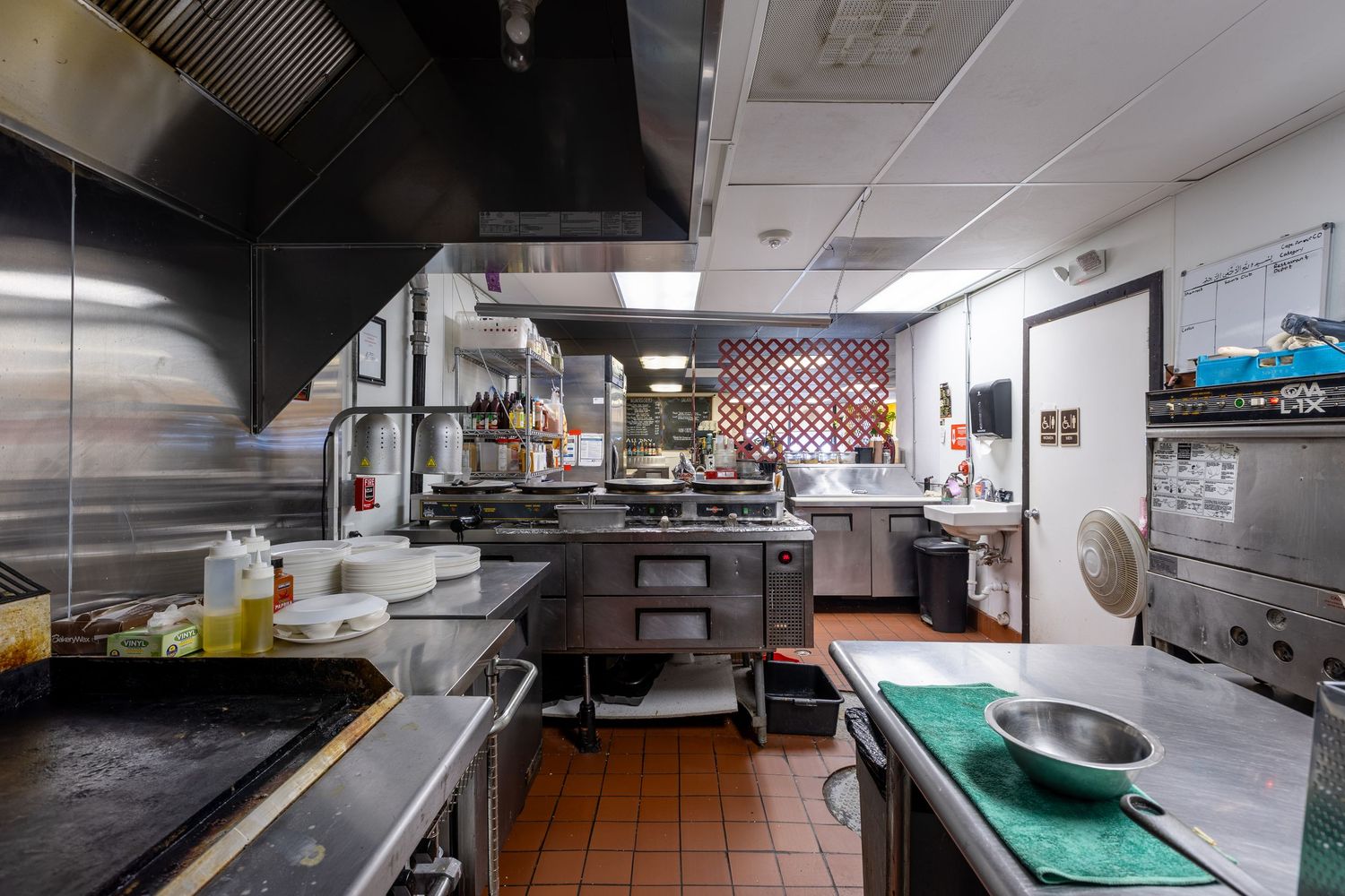 A professional commercial kitchen with stainless steel equipment, prep stations, and ventilation hood in a restaurant setting.