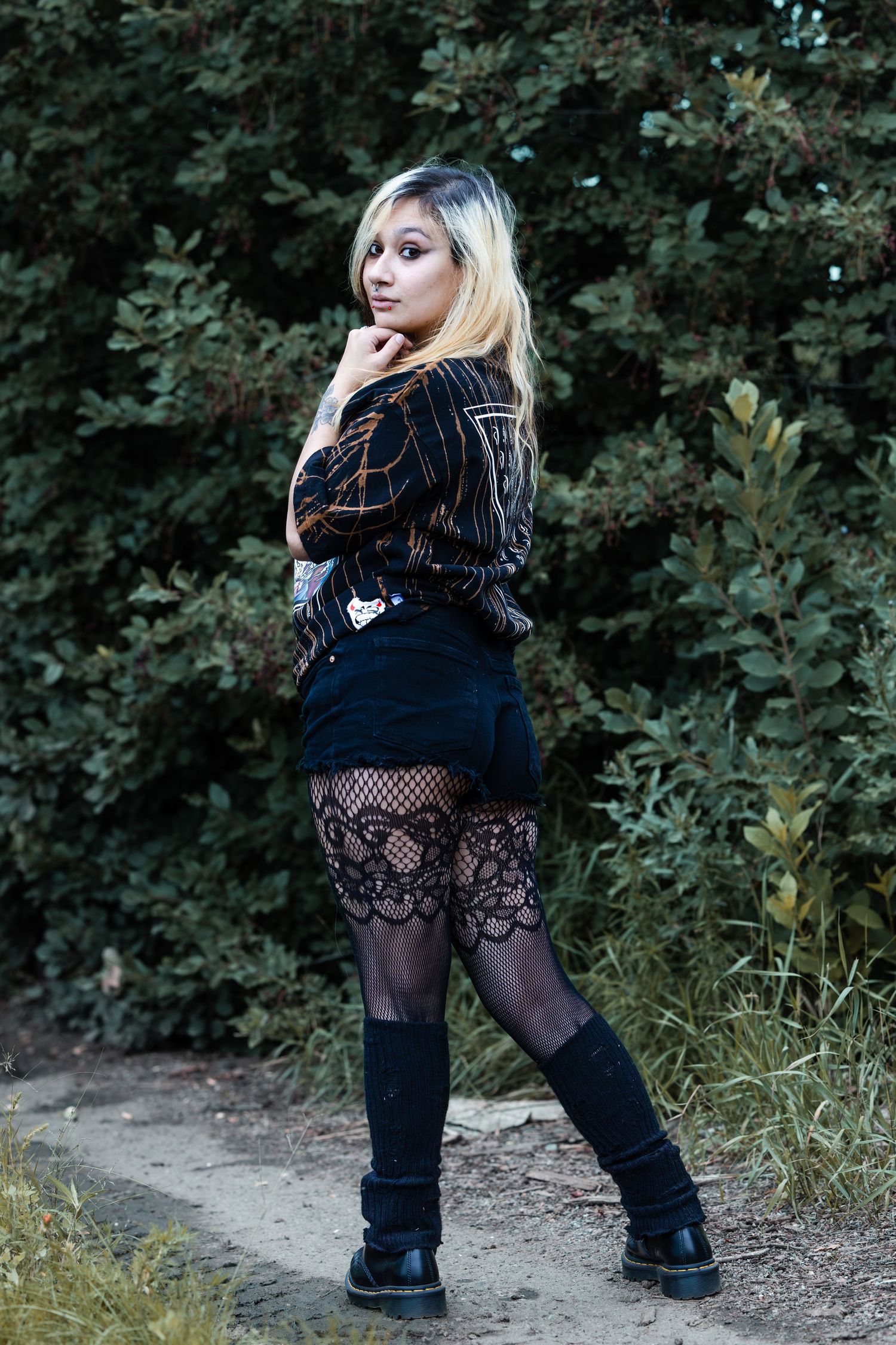 Person wearing black dress and boots poses outdoors on nature trail.