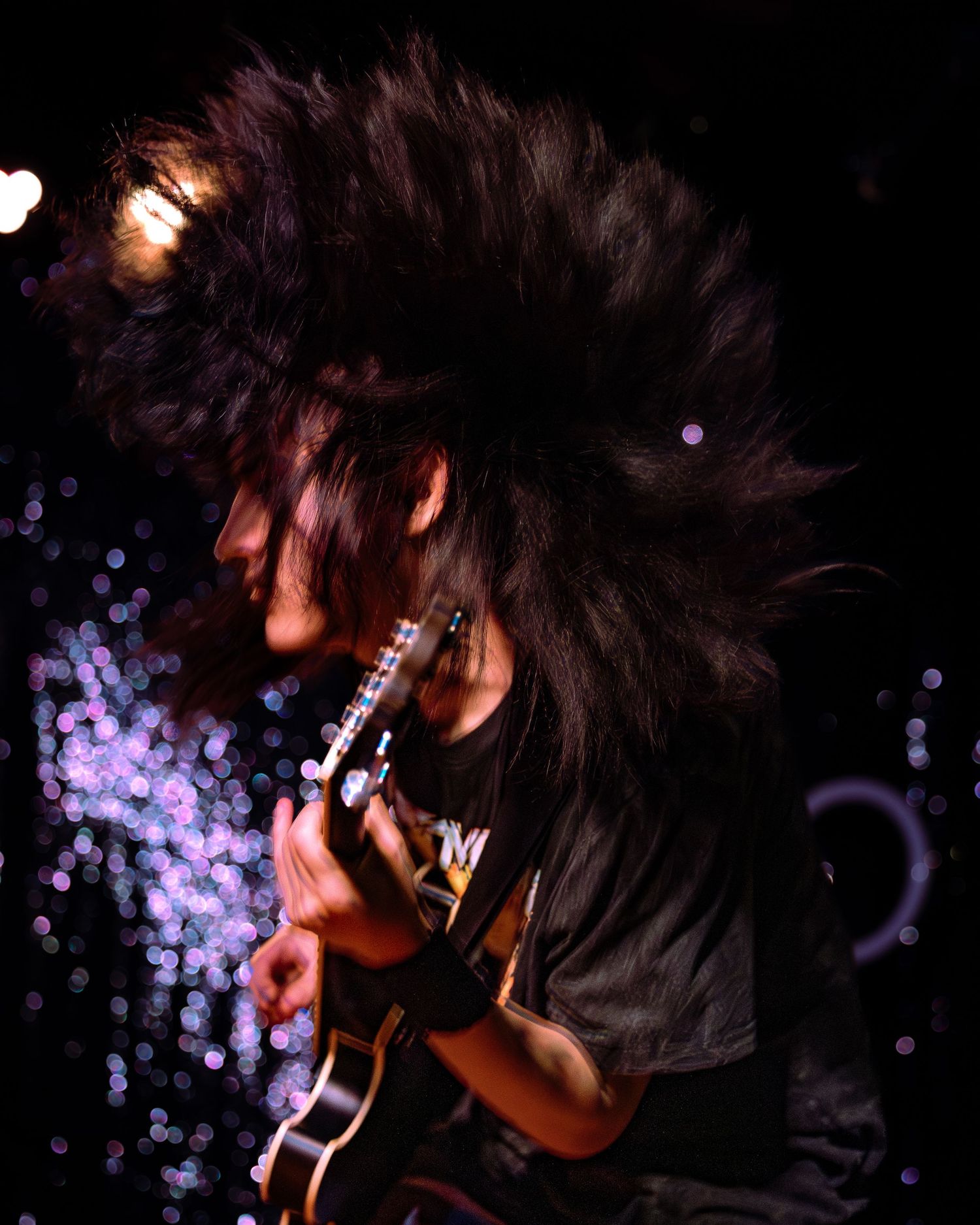 Guitarist headbanging with wild flying hair while playing electric guitar at dark rock concert.