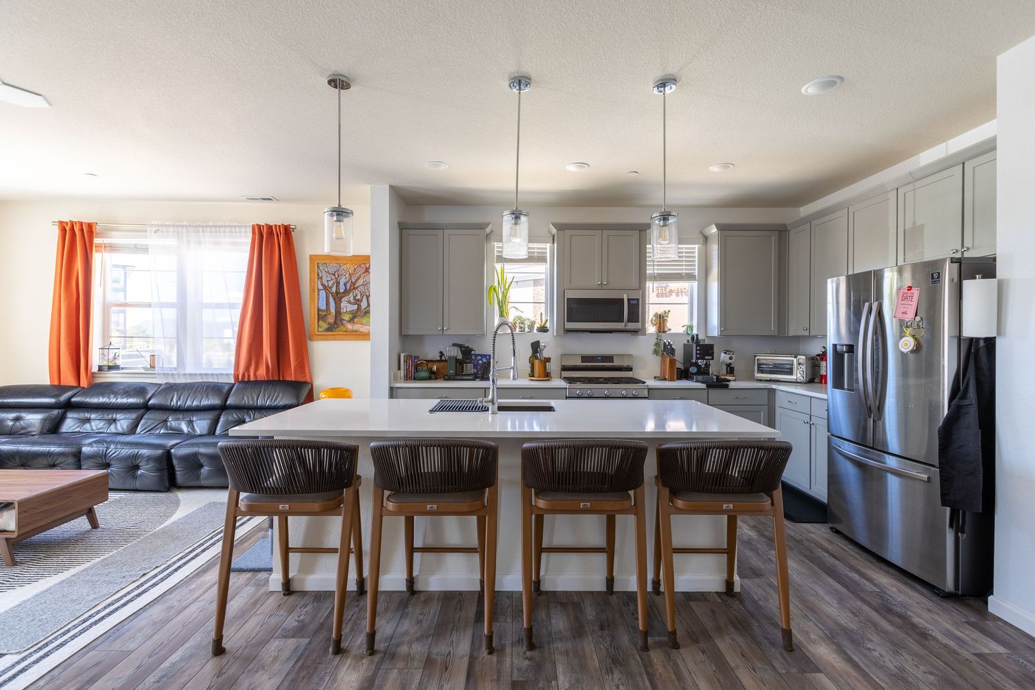 Spacious kitchen featuring gray cabinets, white quartz island, pendant lights, and stainless steel refrigerator.