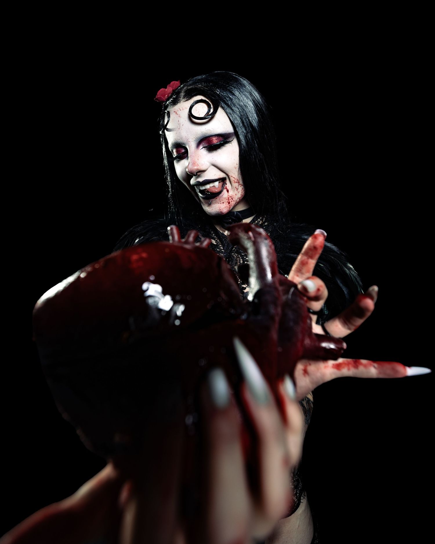 Performer in dramatic vampire makeup with blood effects holds out hand toward camera in dark studio.