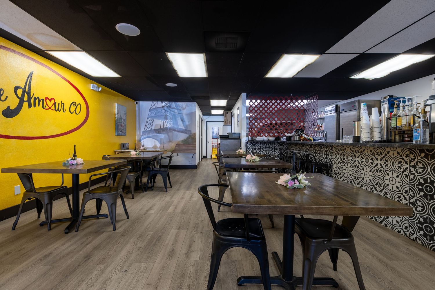 Bright restaurant interior with yellow walls, patterned tiles, wooden tables, and black chairs.