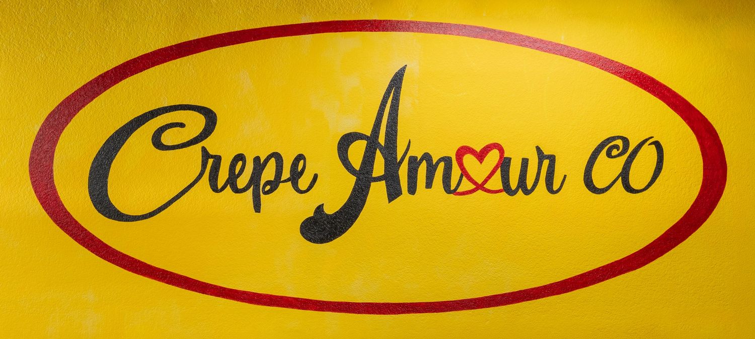 Crepe Amour Co logo on a bright yellow oval sign with red border and decorative script lettering.