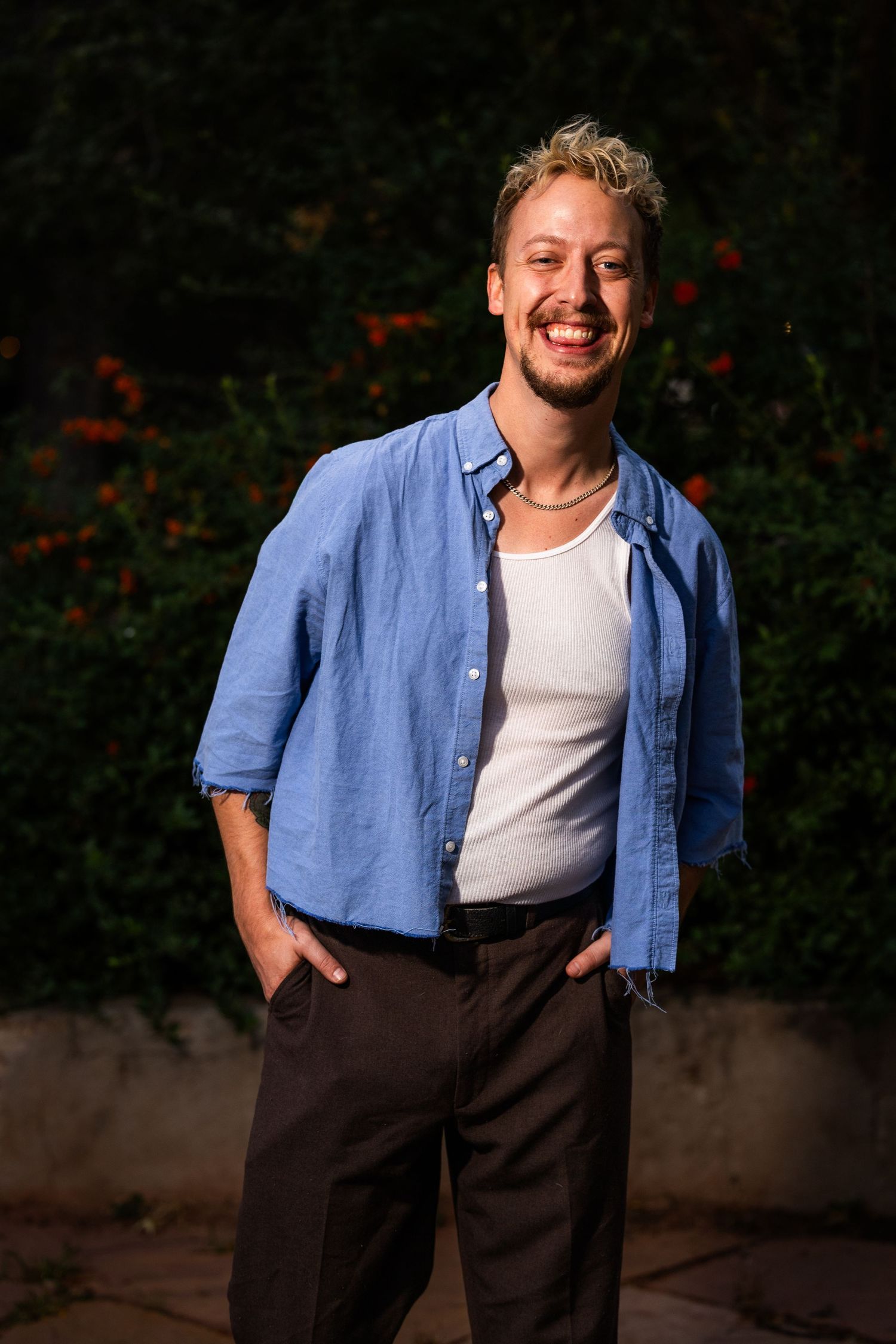 A casual portrait against a dark background showing someone wearing a blue button-down shirt and white undershirt.