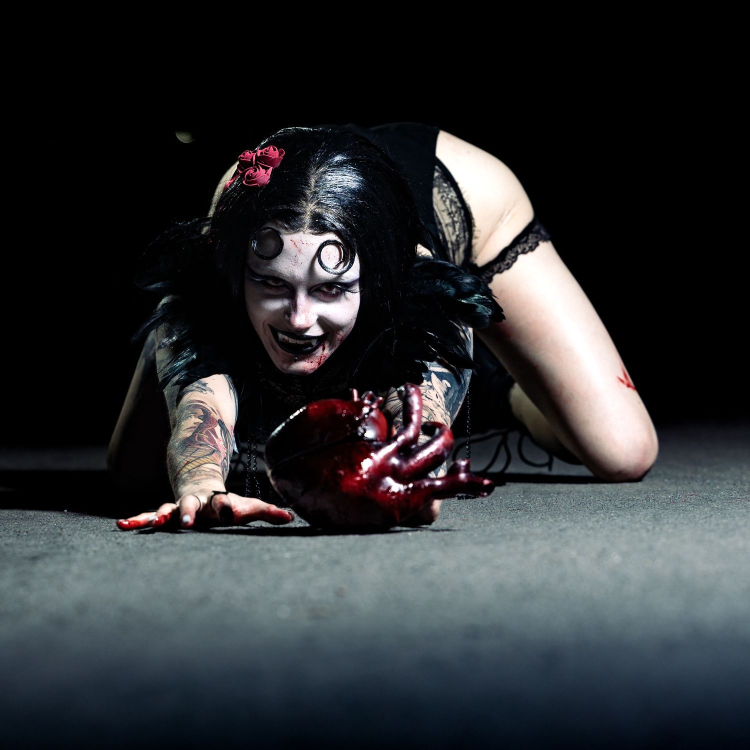 Person in dramatic horror makeup and costume lying on floor with theatrical blood effects in dark studio setting.
