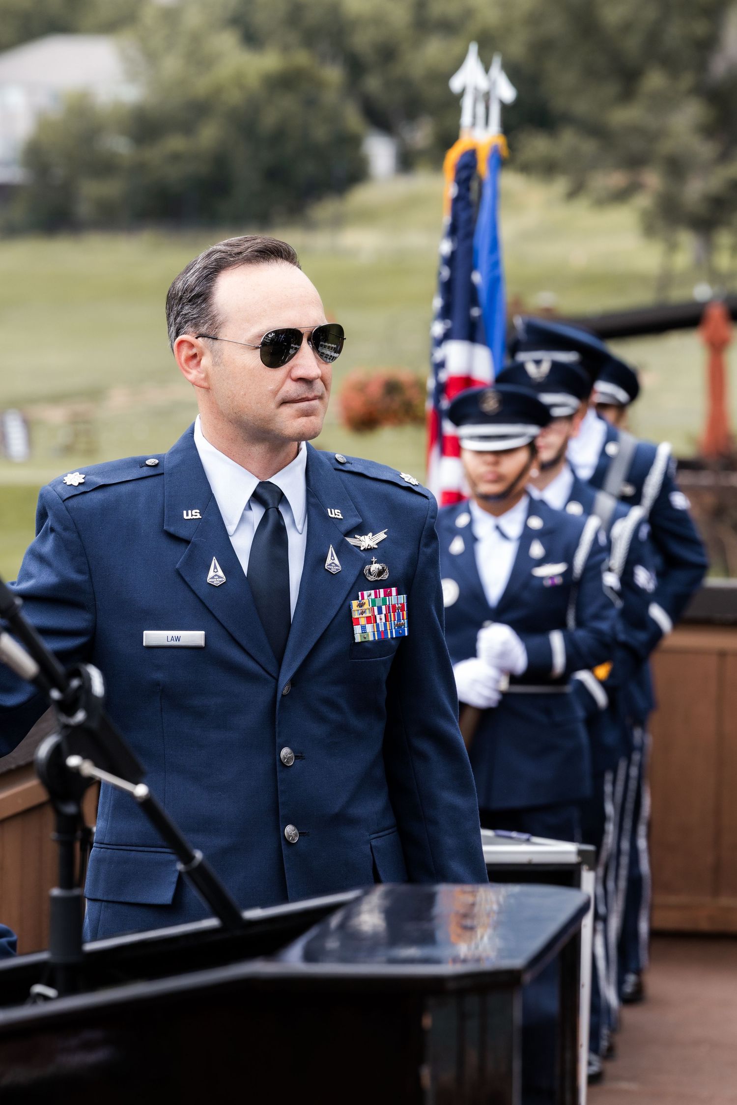 Air Force personnel in dress uniforms stand at attention during outdoor ceremony.
