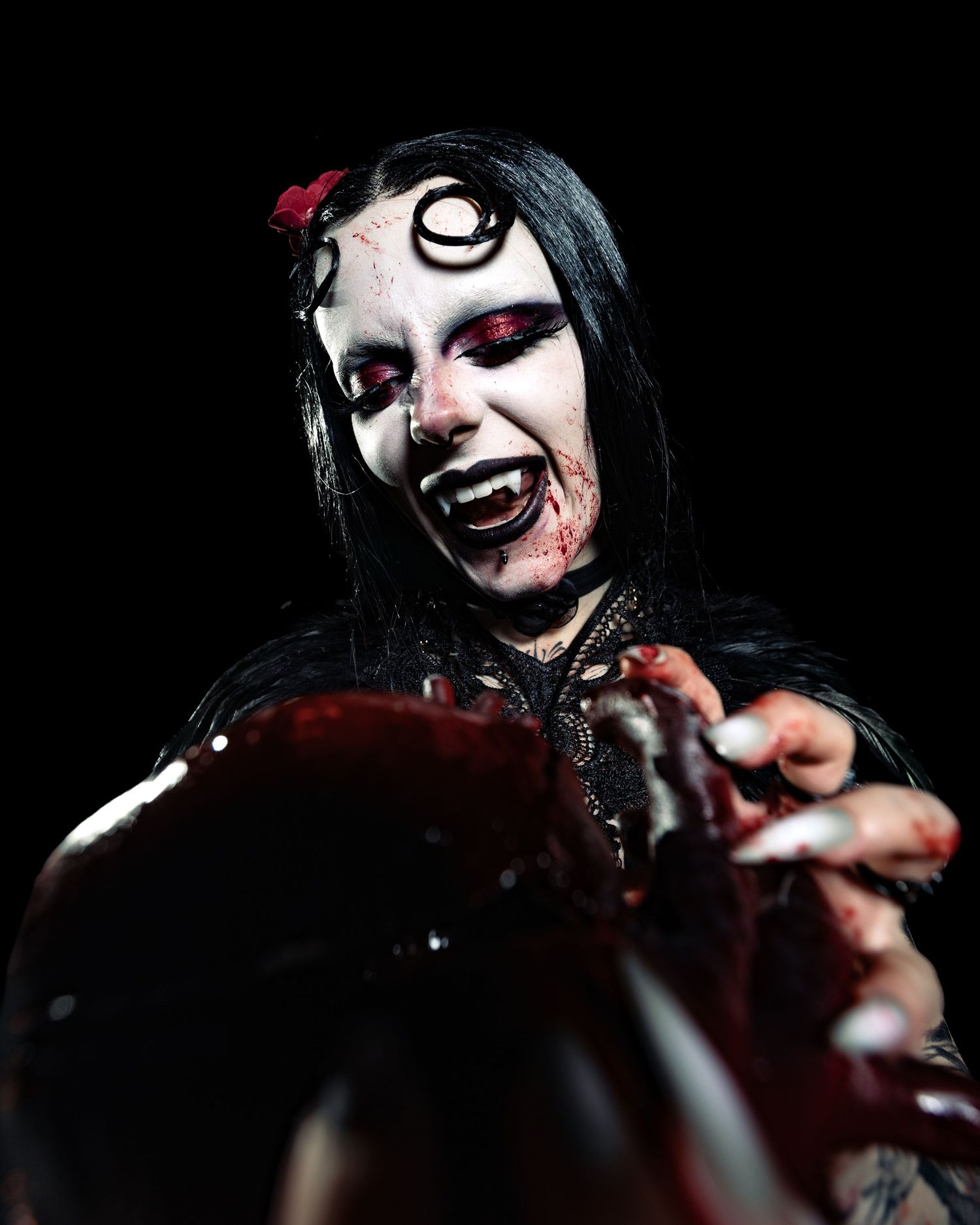 Gothic performer with horror makeup, bloody face paint, and red eyes poses dramatically on dark stage.