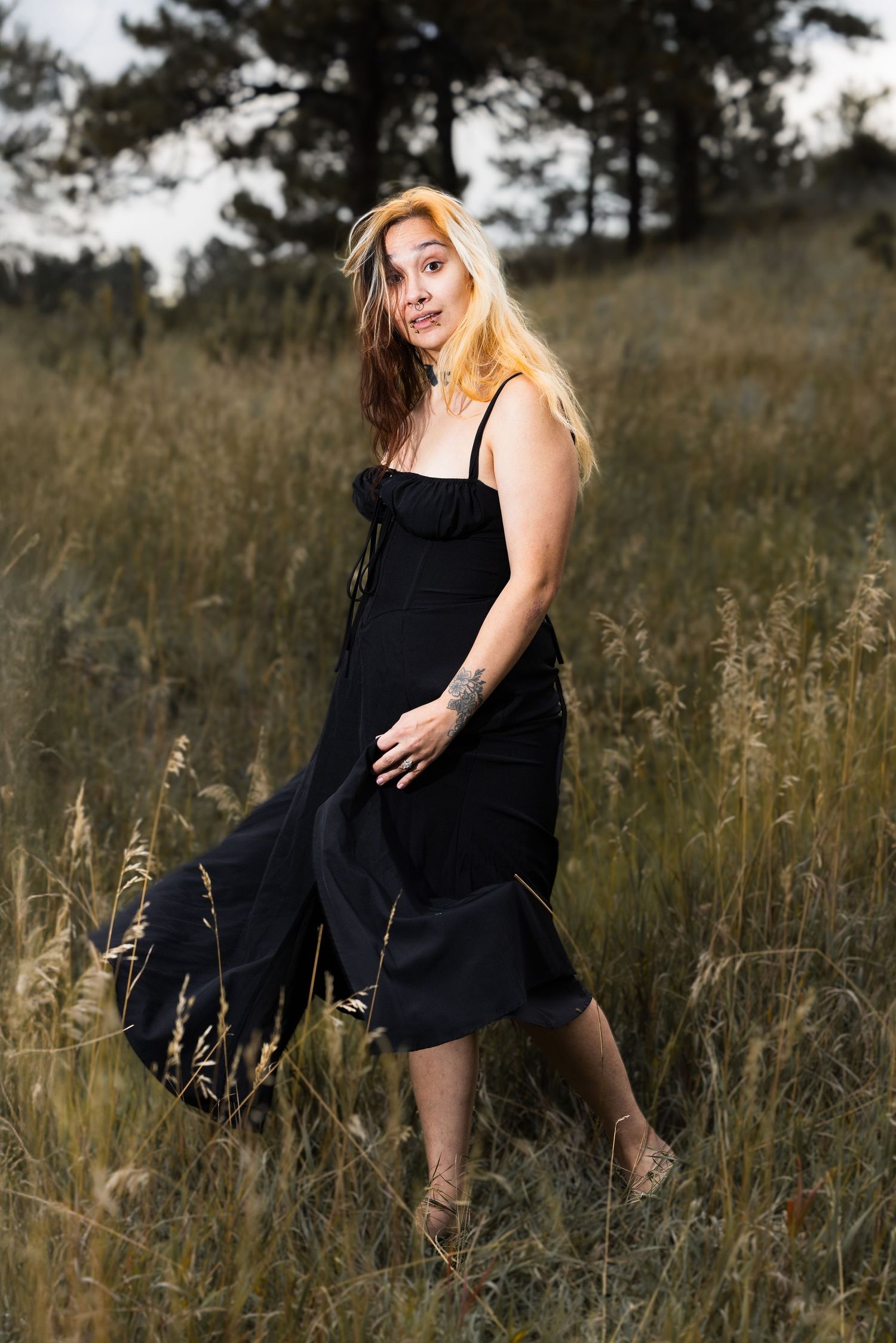 Artistic outdoor photoshoot featuring woman in black dress among wild grasses.