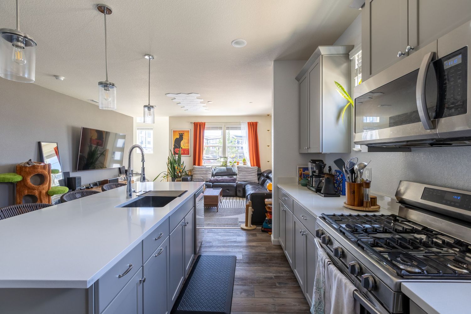 Sleek kitchen with gray cabinets, white quartz countertops, stainless steel appliances, and pendant lights over the sink.