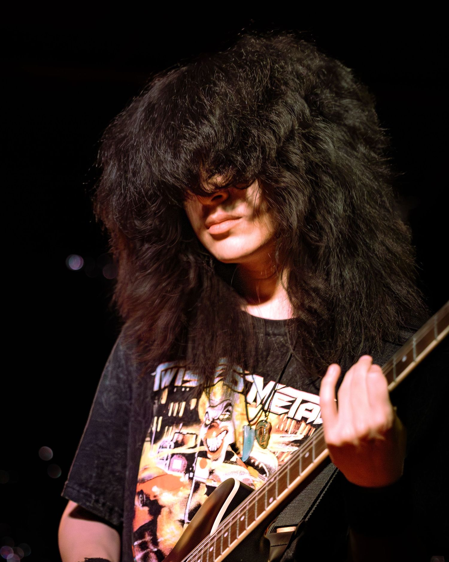 Heavy metal guitarist with voluminous dark hair shredding an electric guitar on stage.