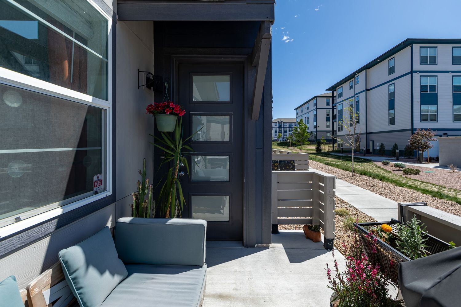 Modern townhouse entrance with gray door, red flowers, and a cozy patio seating area in a contemporary urban community.