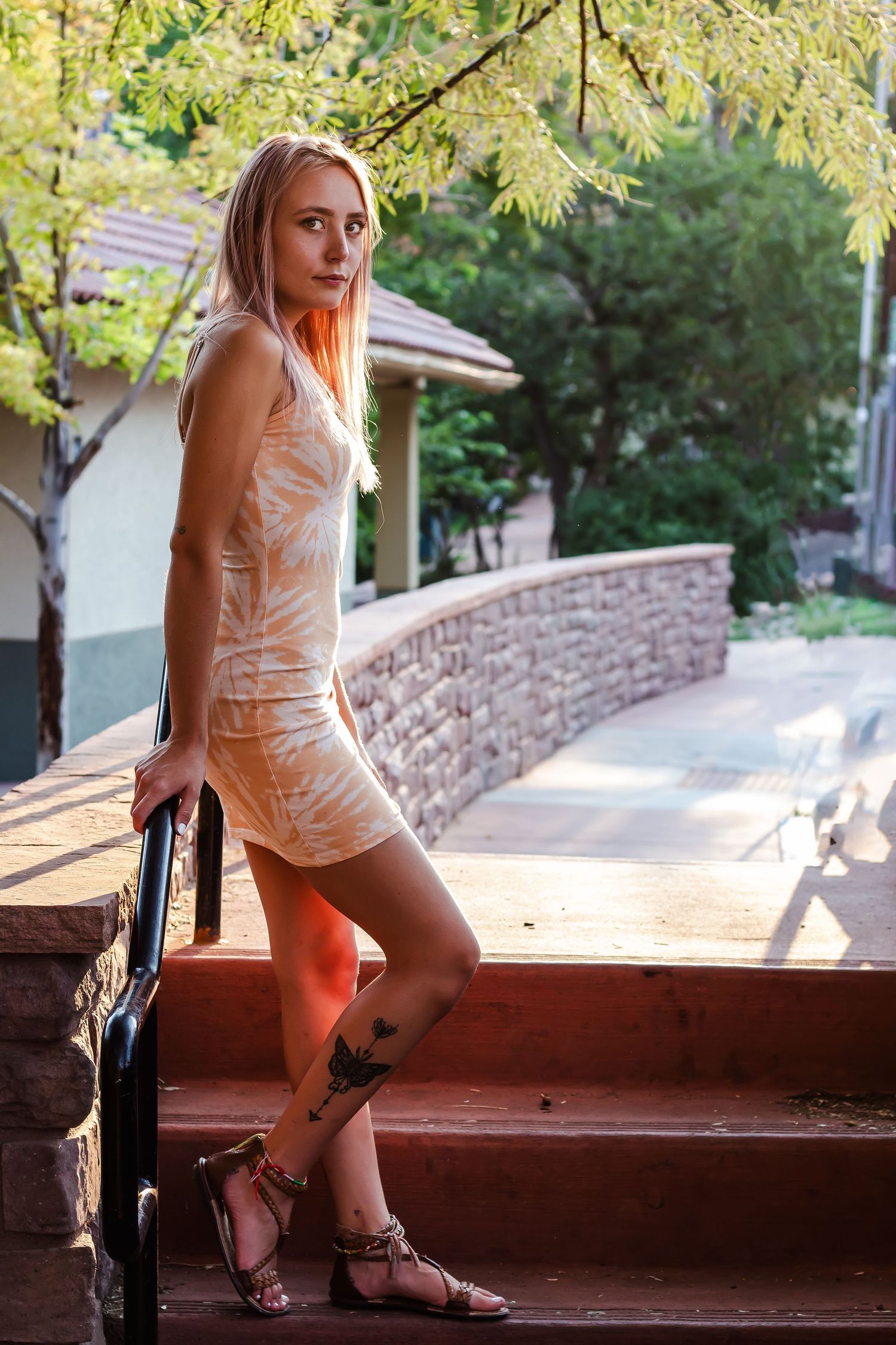 A person in a light colored top and shorts sits on wooden outdoor steps surrounded by green foliage.