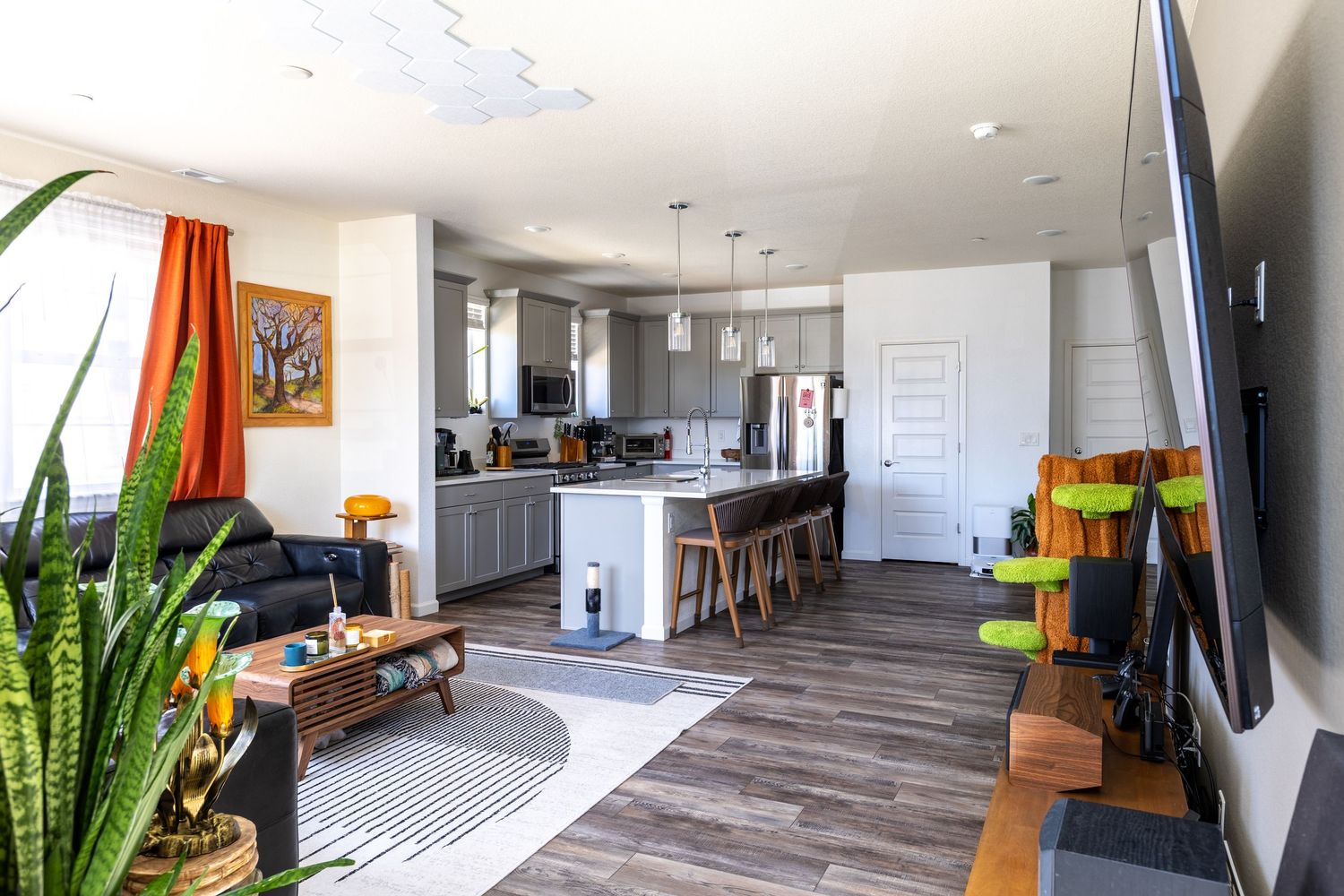 Modern open-concept living room and kitchen with hardwood floors, gray cabinets, kitchen island, and bright natural light.