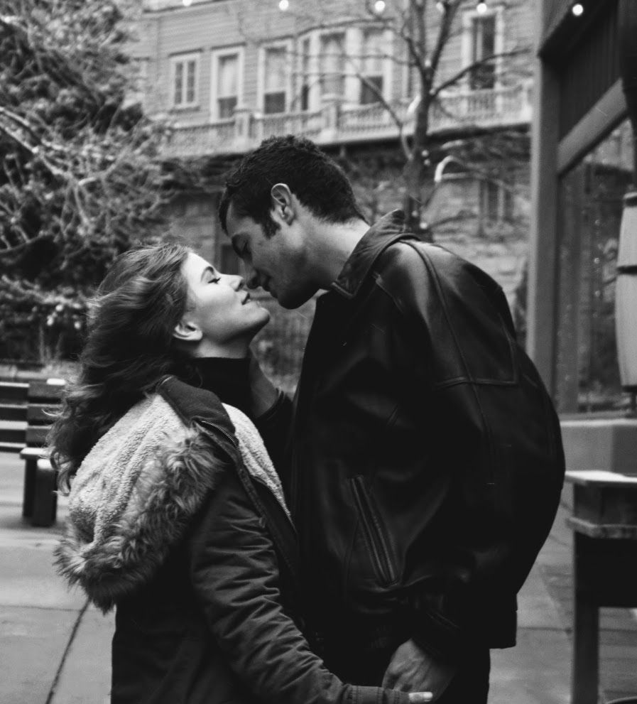 A black and white photograph captures an intimate moment between two people on an urban street.