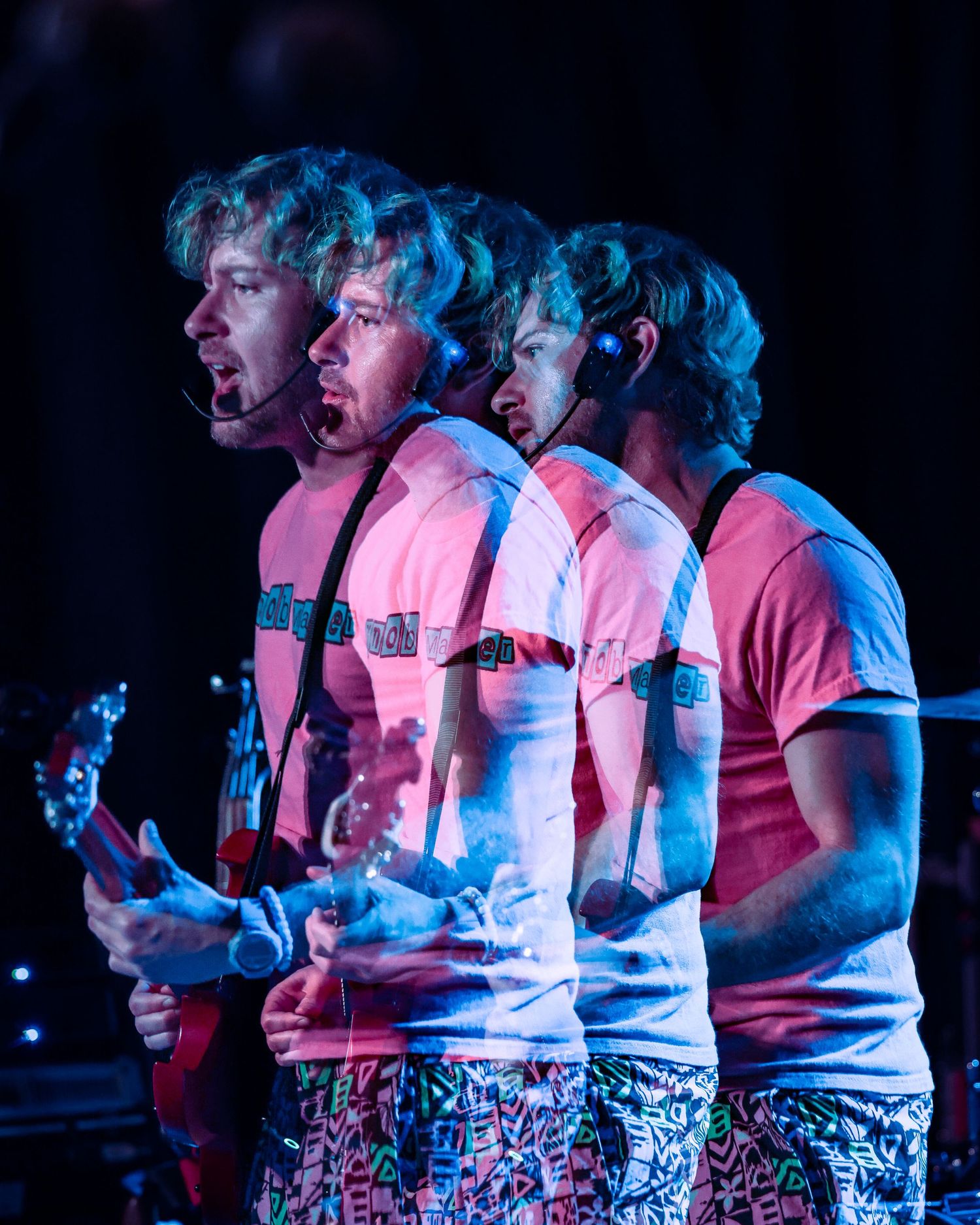 Creative multiple exposure photo of guitarist in pink shirt performing live on stage.