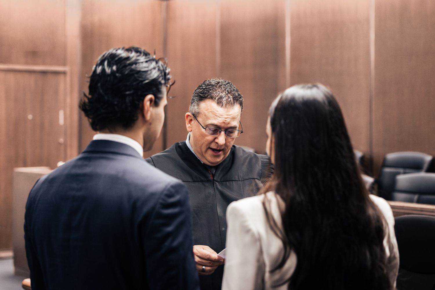 Judge in black robe consults with two attorneys in a courtroom setting during a legal proceeding.