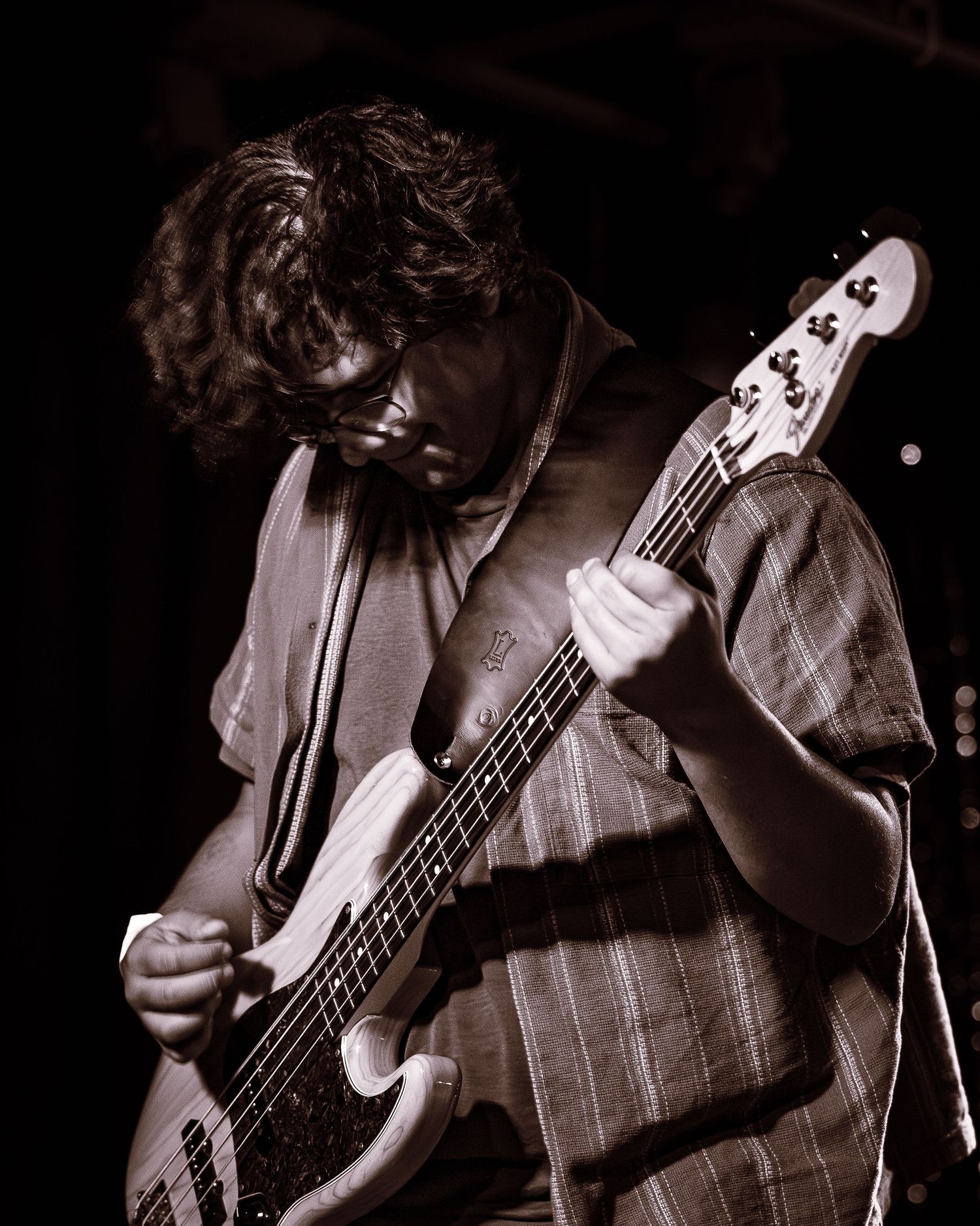 Young male guitarist playing bass guitar on stage in a moody sepia-toned performance photo.